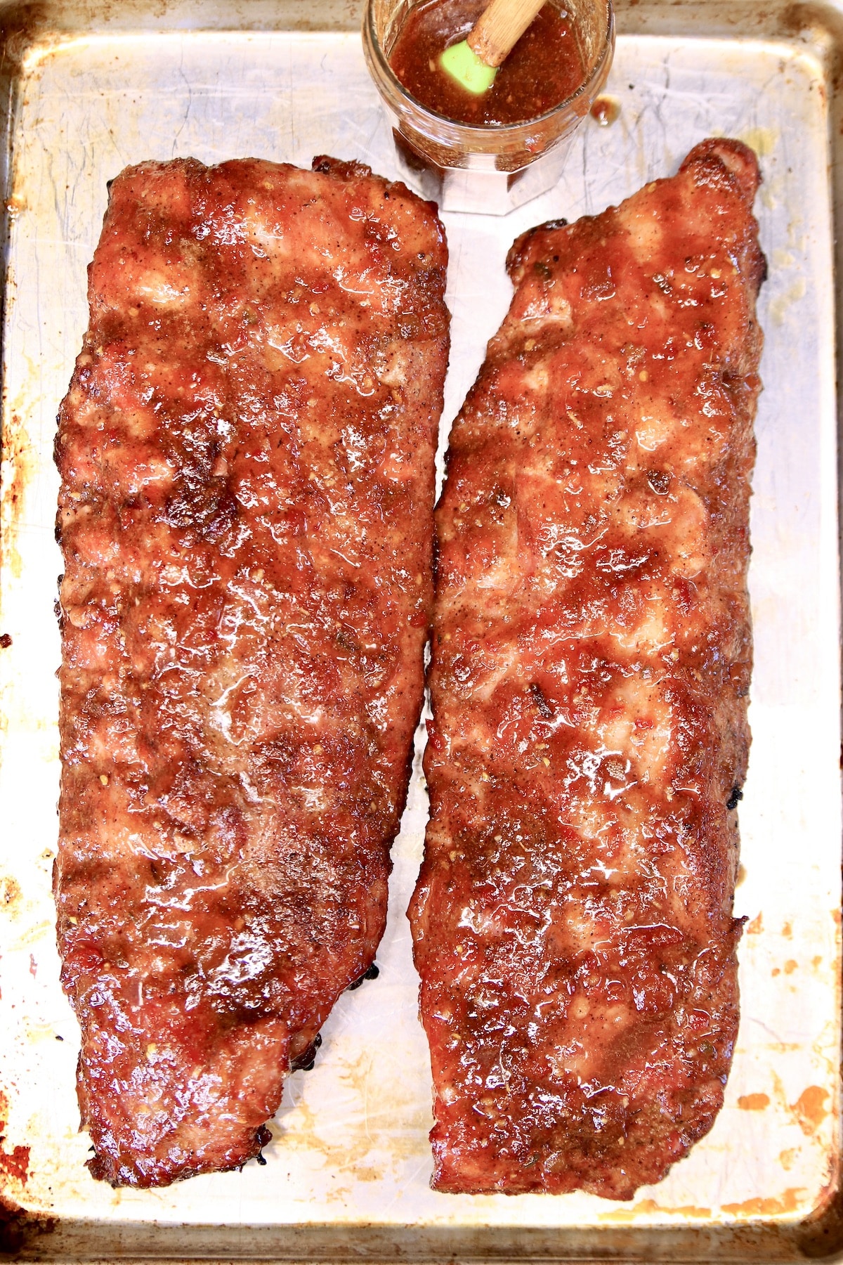 2 racks grilled baby back ribs on a baking sheet with jar of sauce.