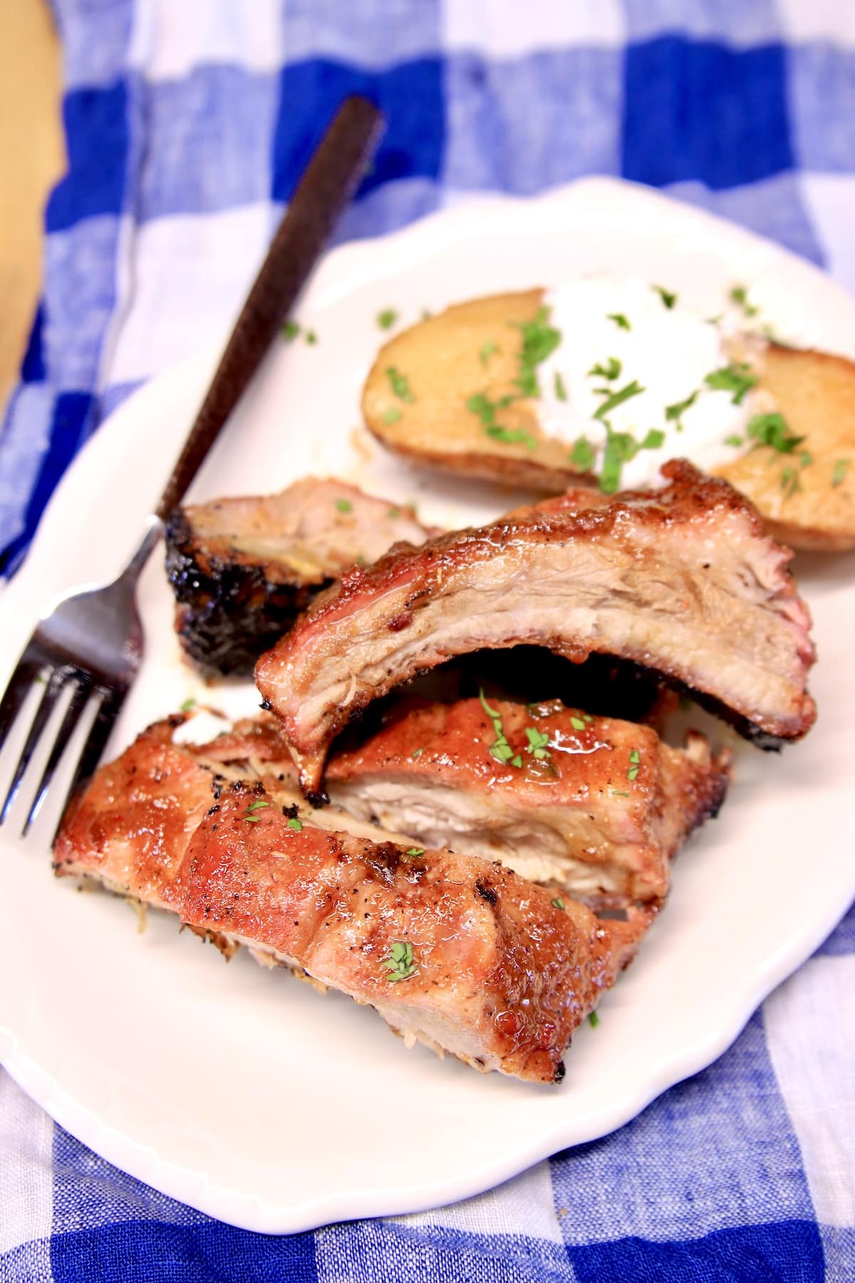 Plate with 3 baby back ribs, baked potato with sour cream.