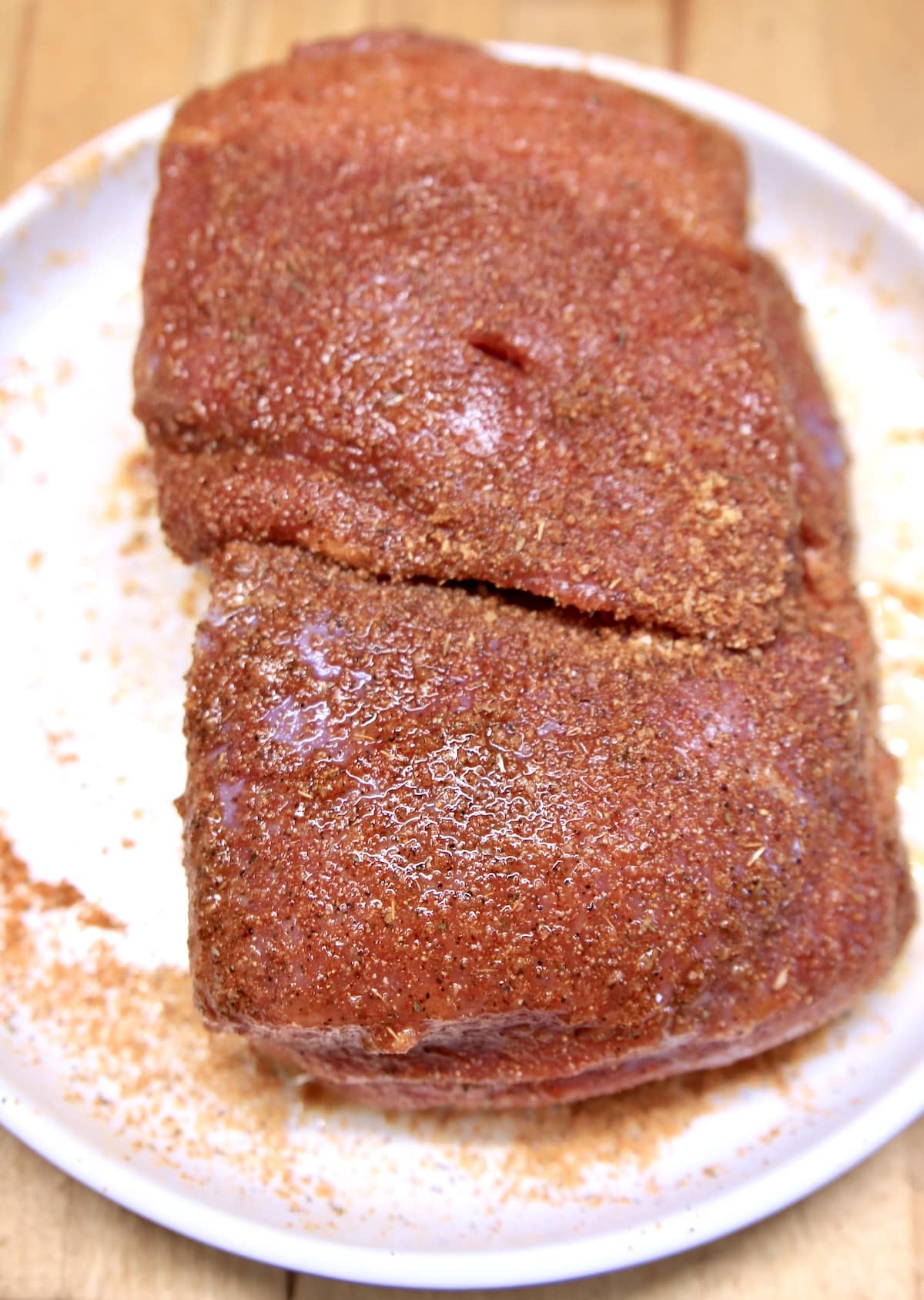Raw venison roast seasoned with dry rub on a sheet pan.