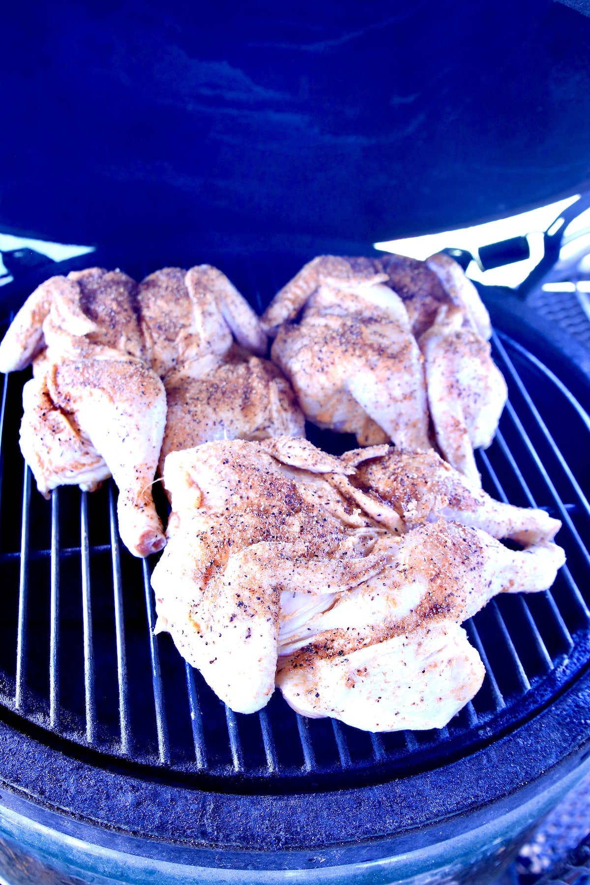 3 spatchcock chickens on a grill.