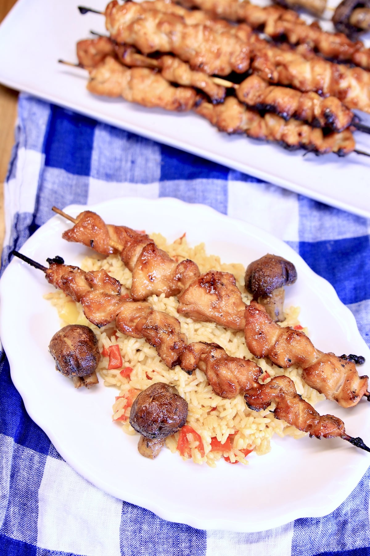 Chicken teriyaki skewers on a plate with mushrooms and rice.