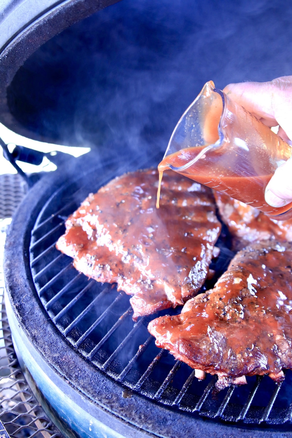 Pouring BBQ sauce over spare ribs on a grill.