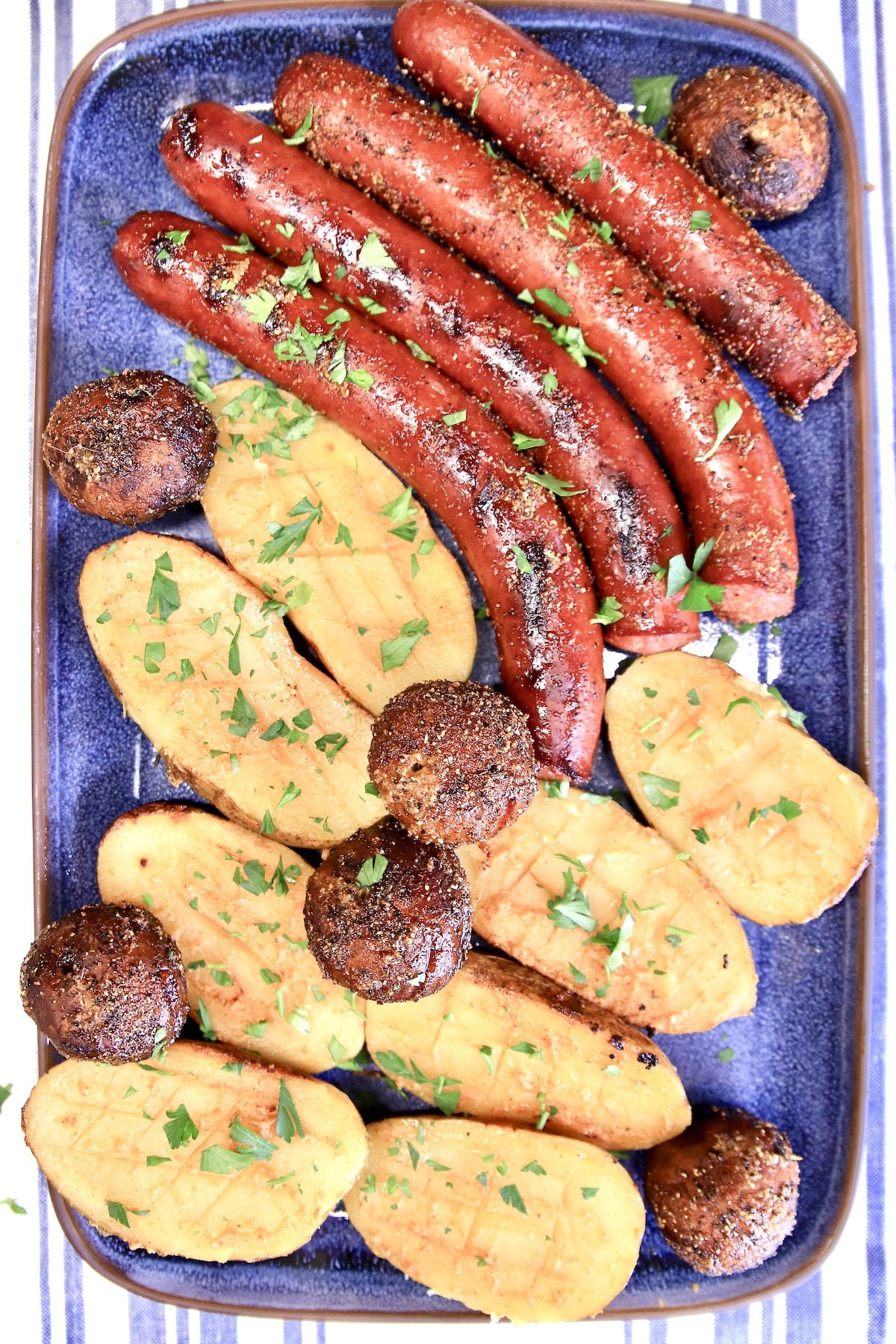 Platter with grilled smoked sausage links, mushrooms, baked potato halves.