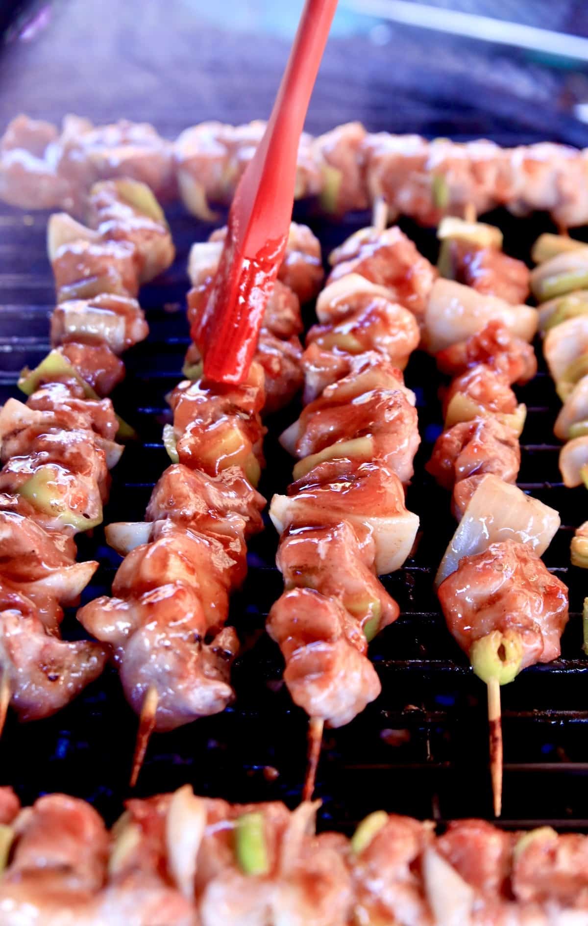 Brushing plum sauce over kabobs on a grill.