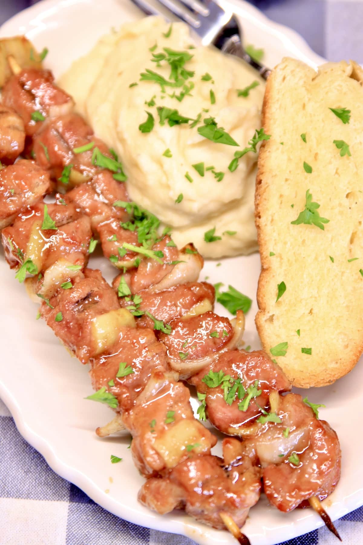 Grilled pork kabobs on a plate with mashed potatoes and garlic bread.