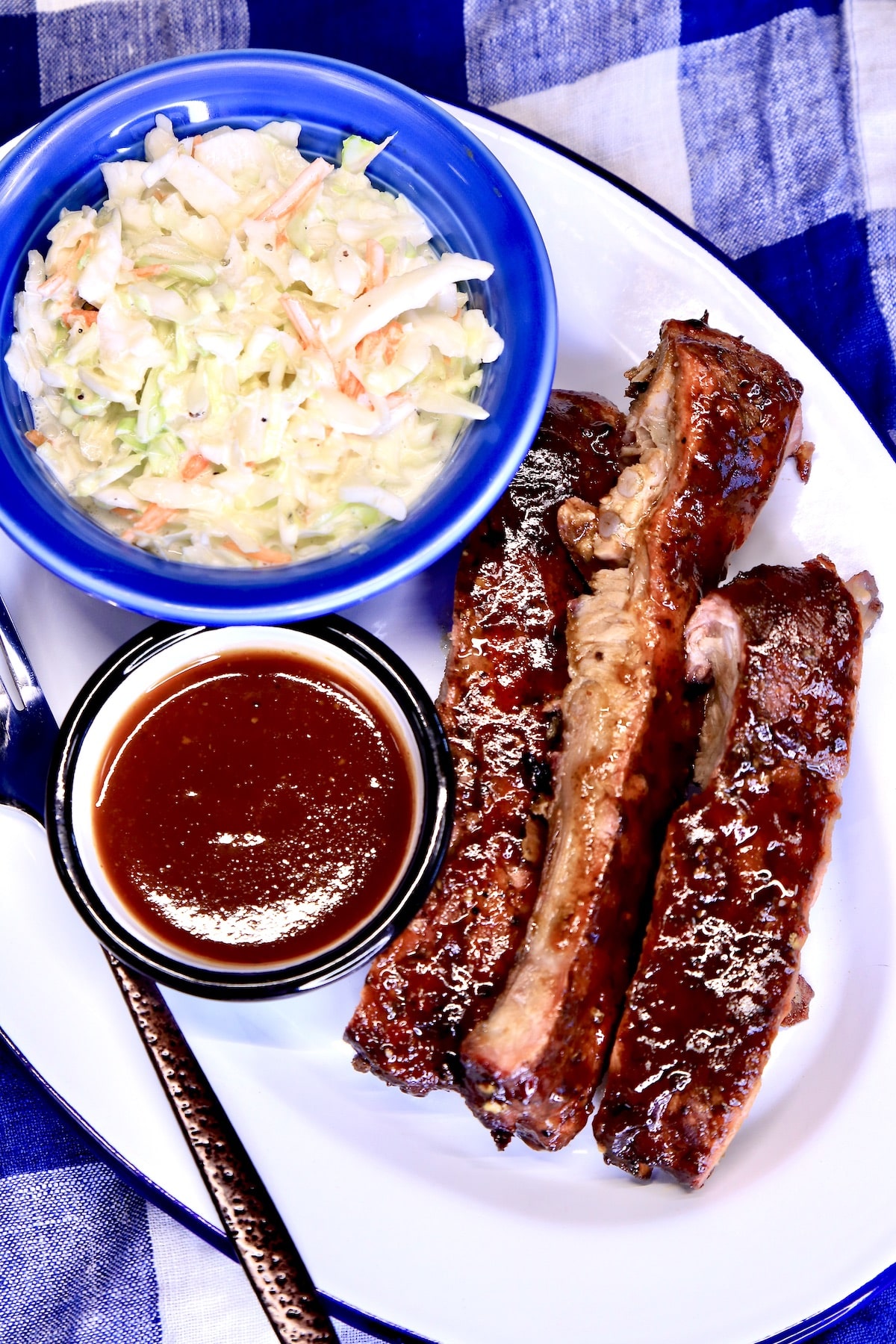 Platter with bbq ribs, bowl of slaw, bowl of sauce.