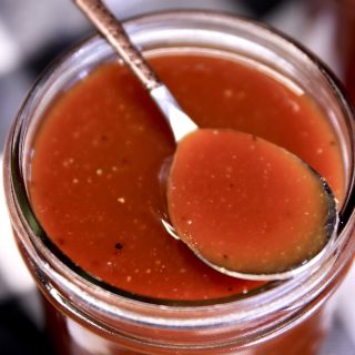 Jar of BBQ sauce with a spoonful on top.