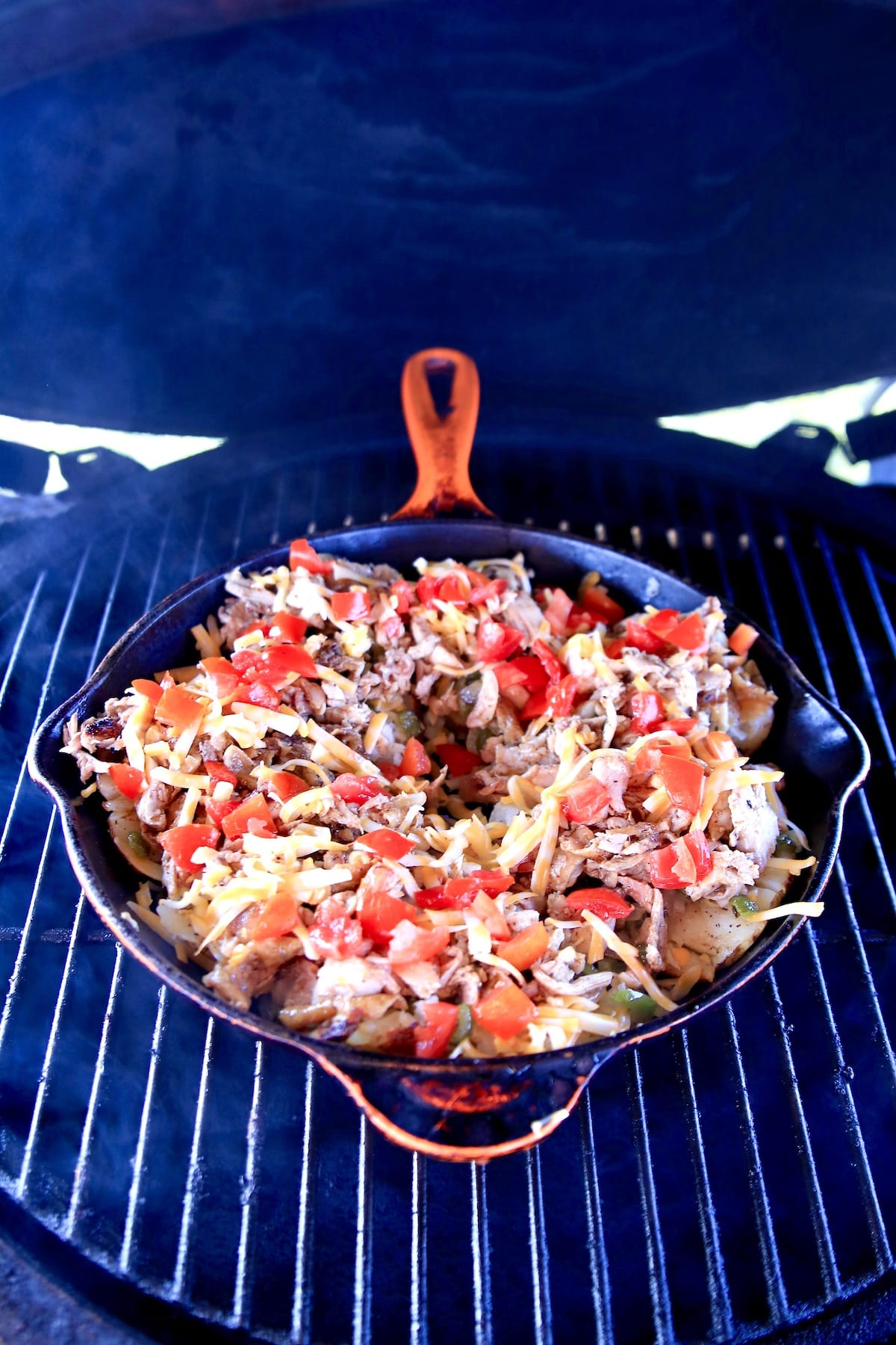 Skillet with chicken stuffed potatoes on a grill.