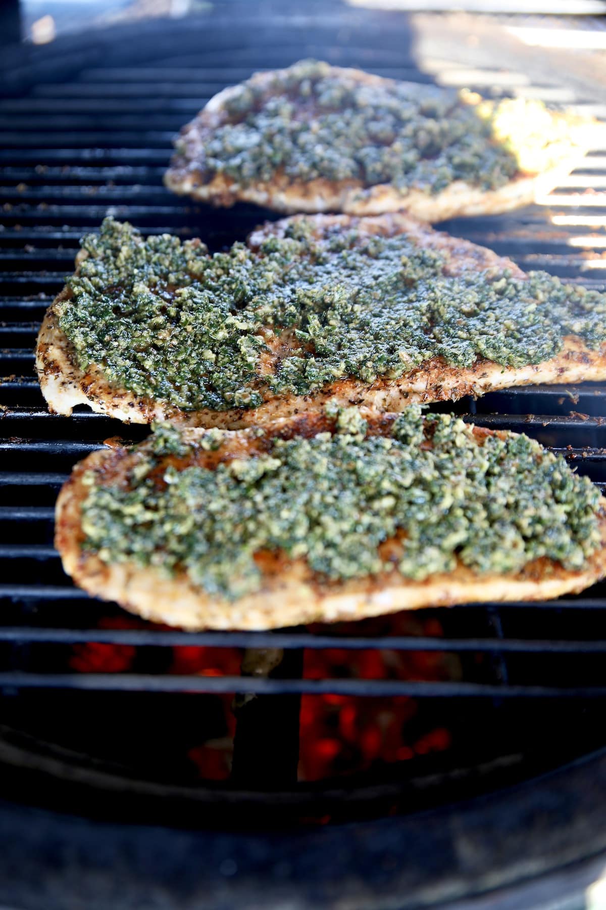 Pesto on chicken cutlets, on a grill.