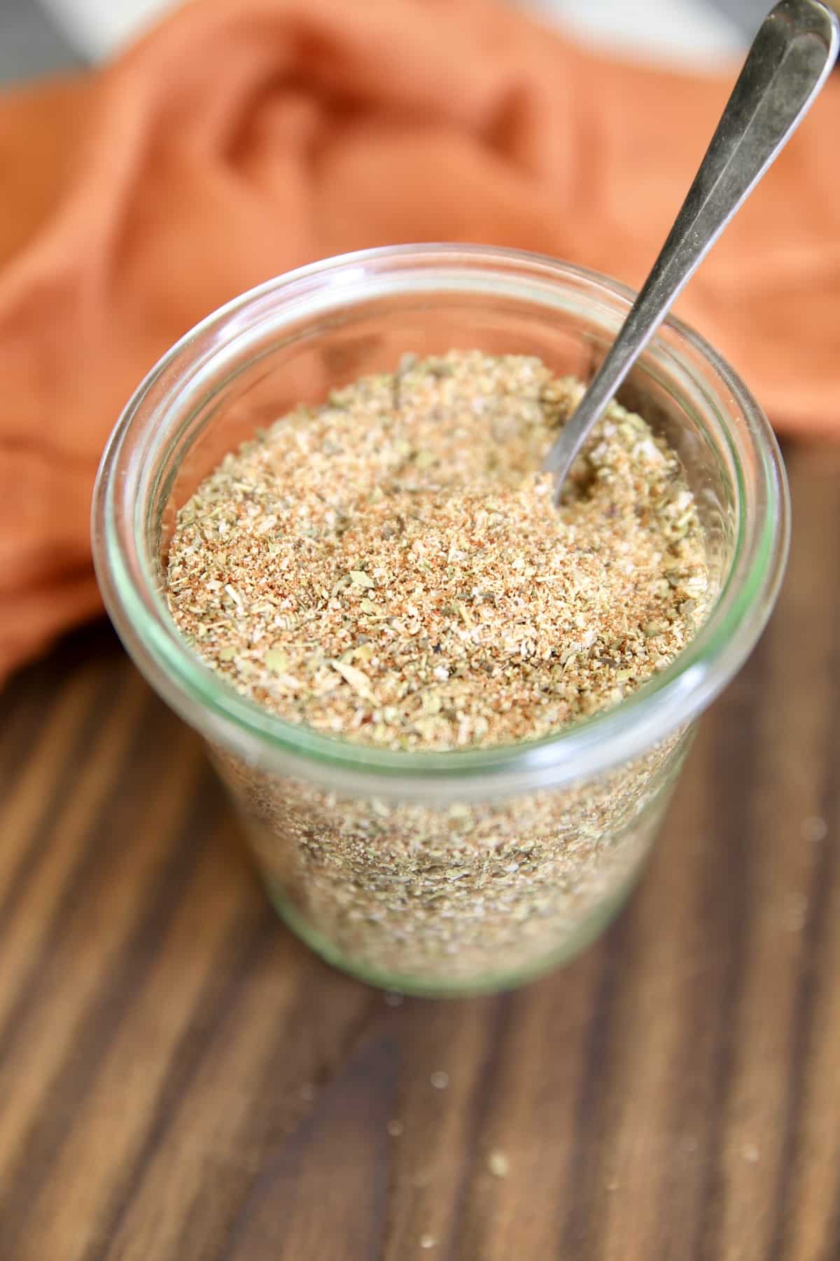 Jar of spice rub on a board with spoon in the jar.