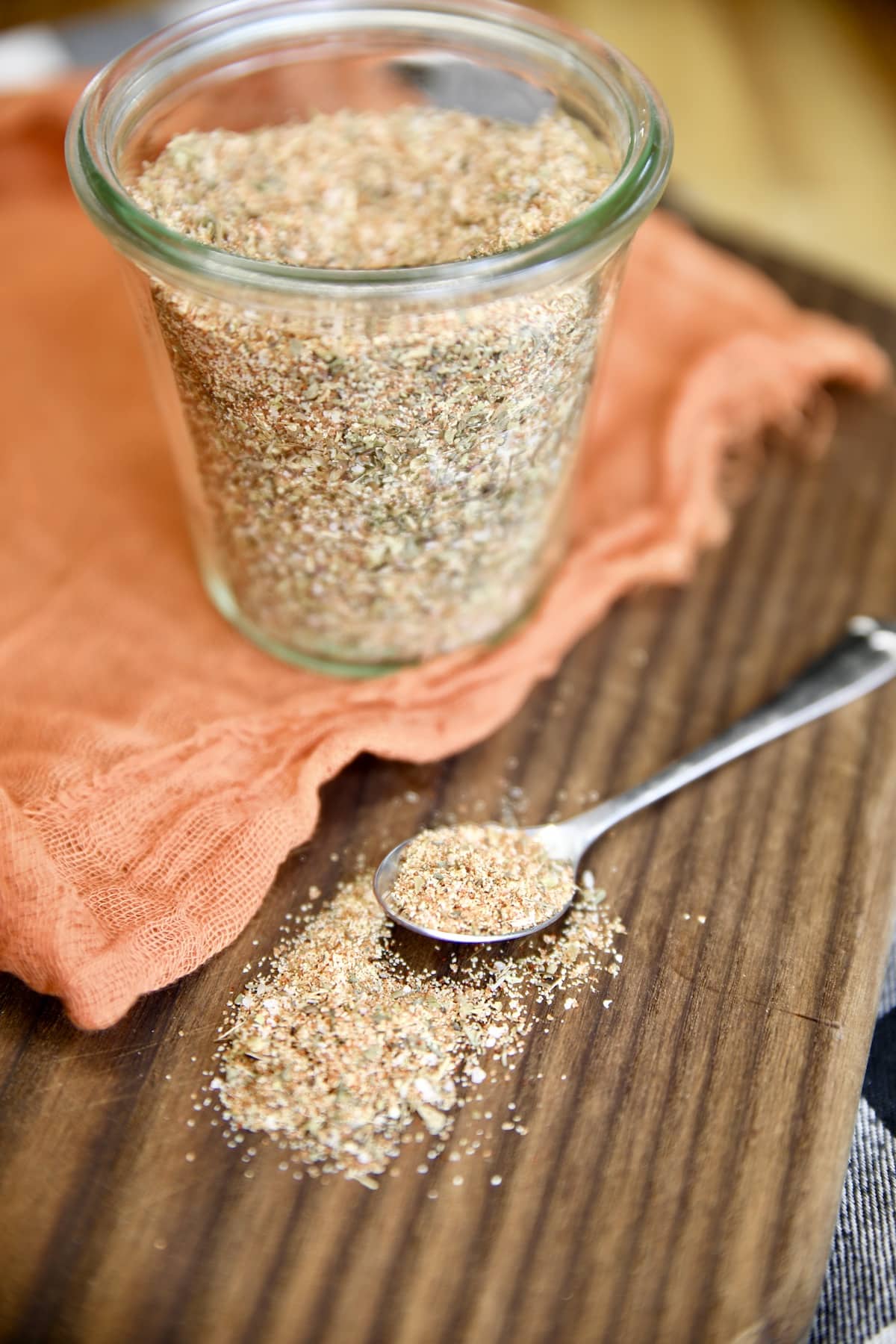 Jar of spice rub, spoonful spilled onto board.