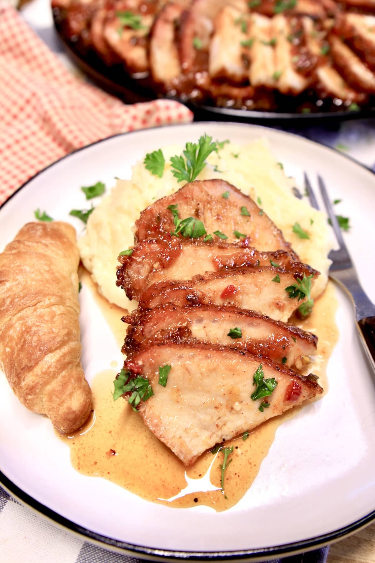 Sliced pork loin on a plate with mashed potatoes and crescent roll.