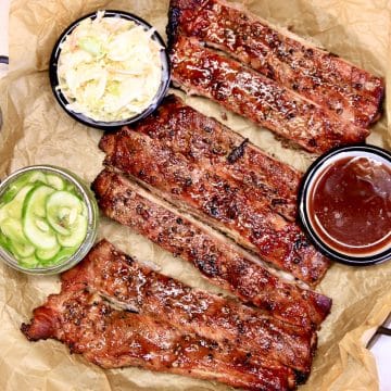 Plum glazed spare ribs on a tray with sauce, slaw and pickles.