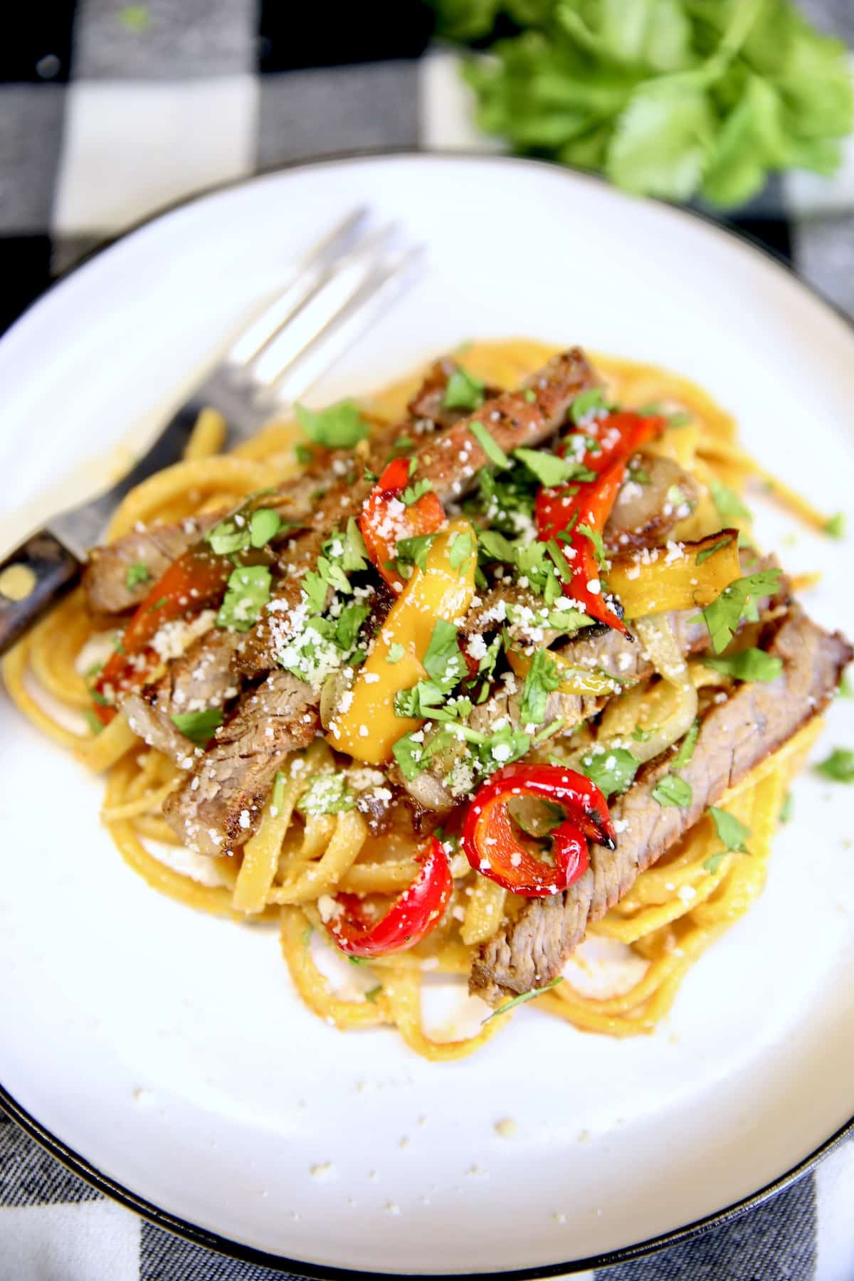 Plate of pasta with sliced steak, peppers, onions.