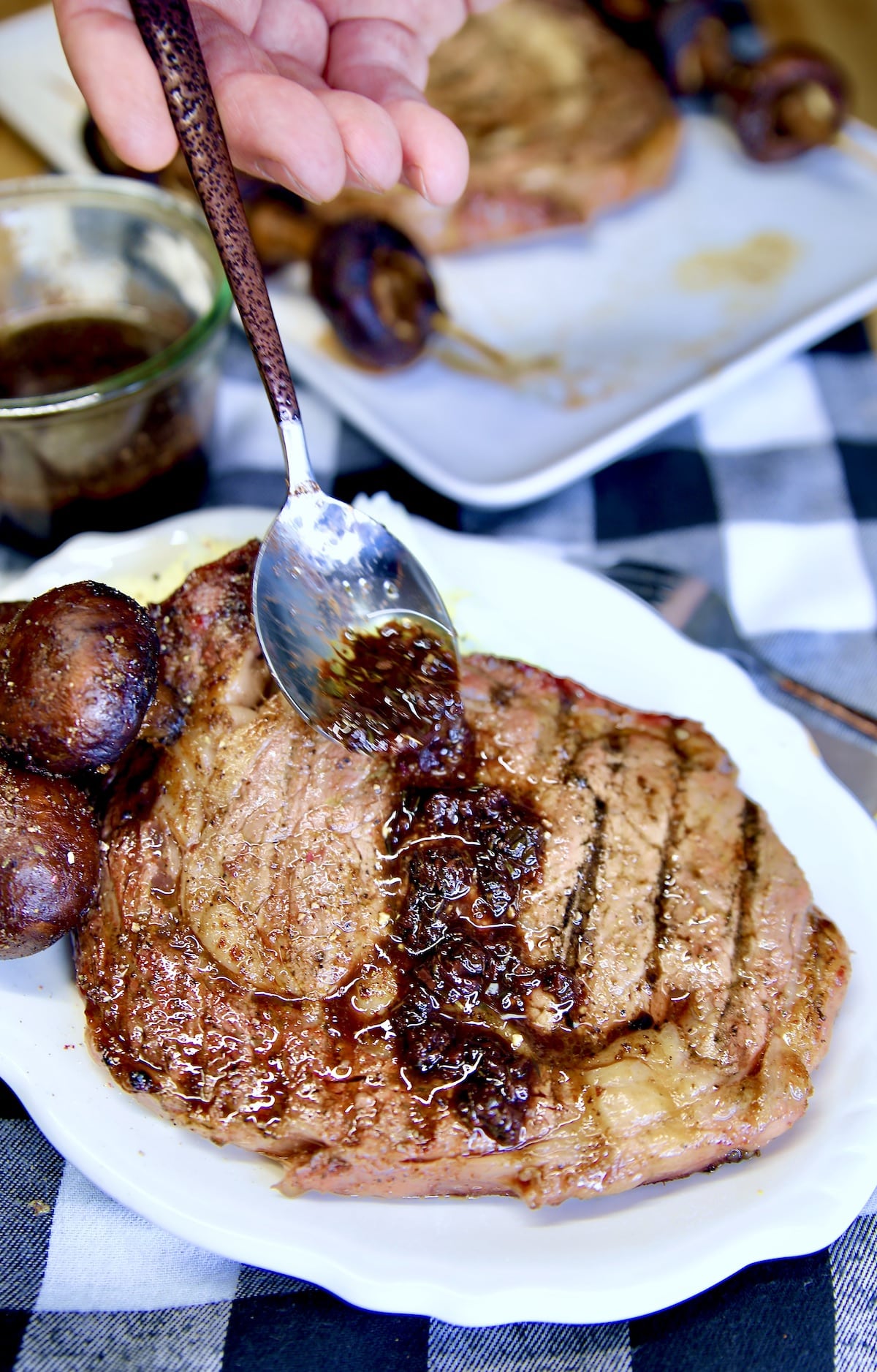 Spooning red wine sauce over ribeye steak on a plate.