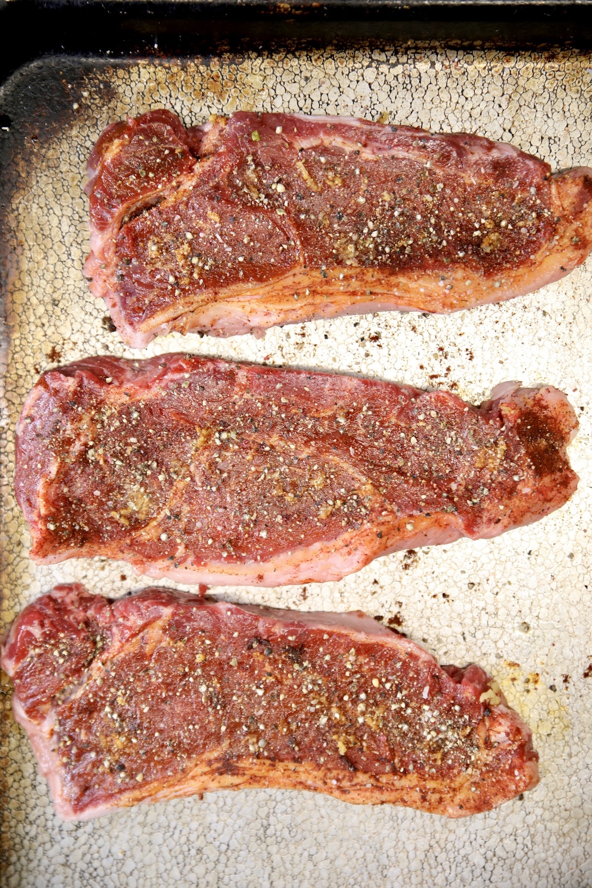Seasoned strip steaks ready to grill.