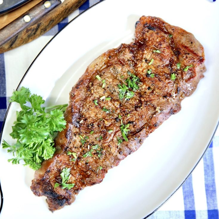 Grilled strip steak on a platter, parsley garnish.
