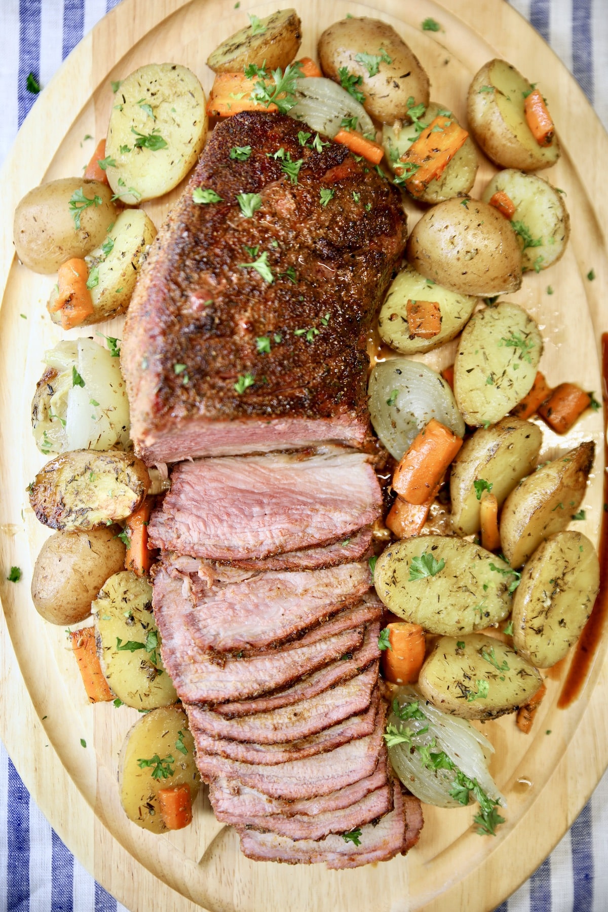 Oval cutting board with roast beef, partially sliced, roasted carrots, potatoes, onions.