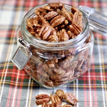 Open jar of candied pecans on a plaid cloth.
