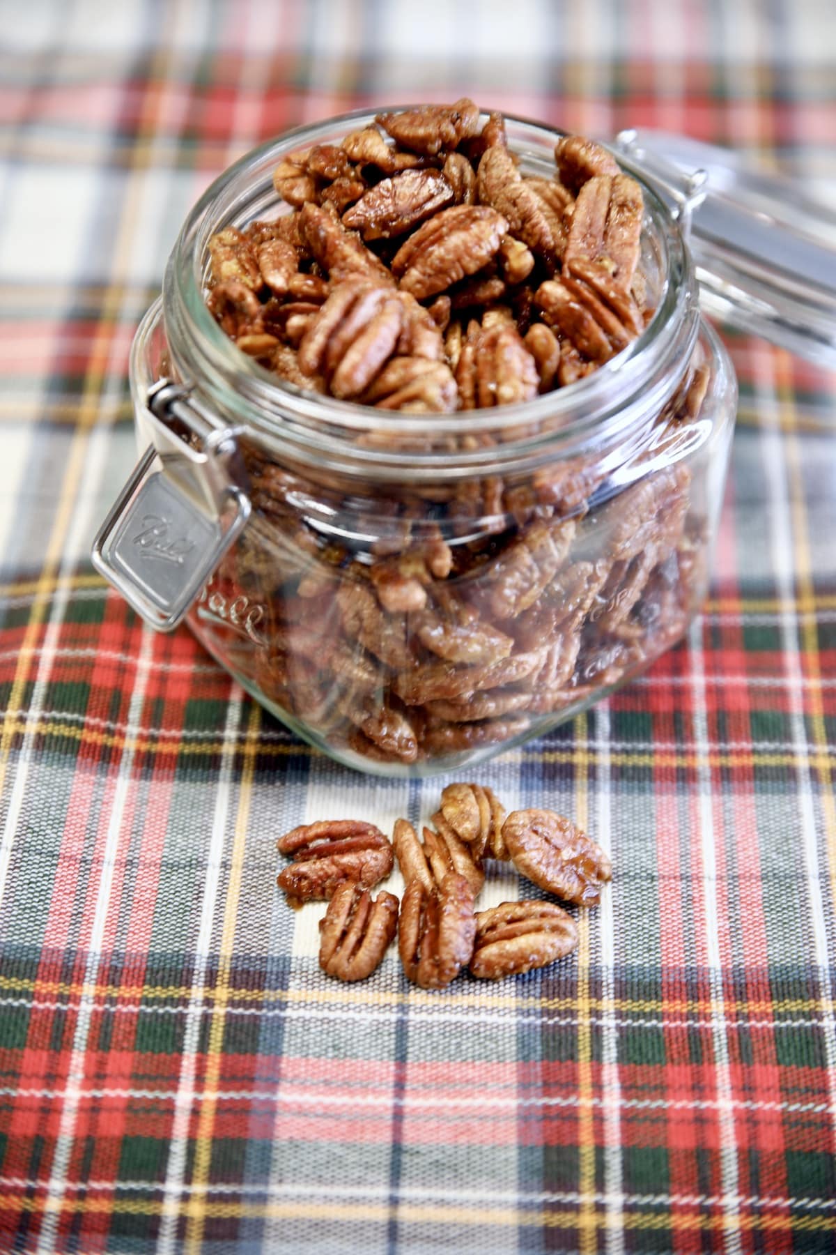 Candied pecans in a jar on a Christmas plaid cloth, a few pecans in front.