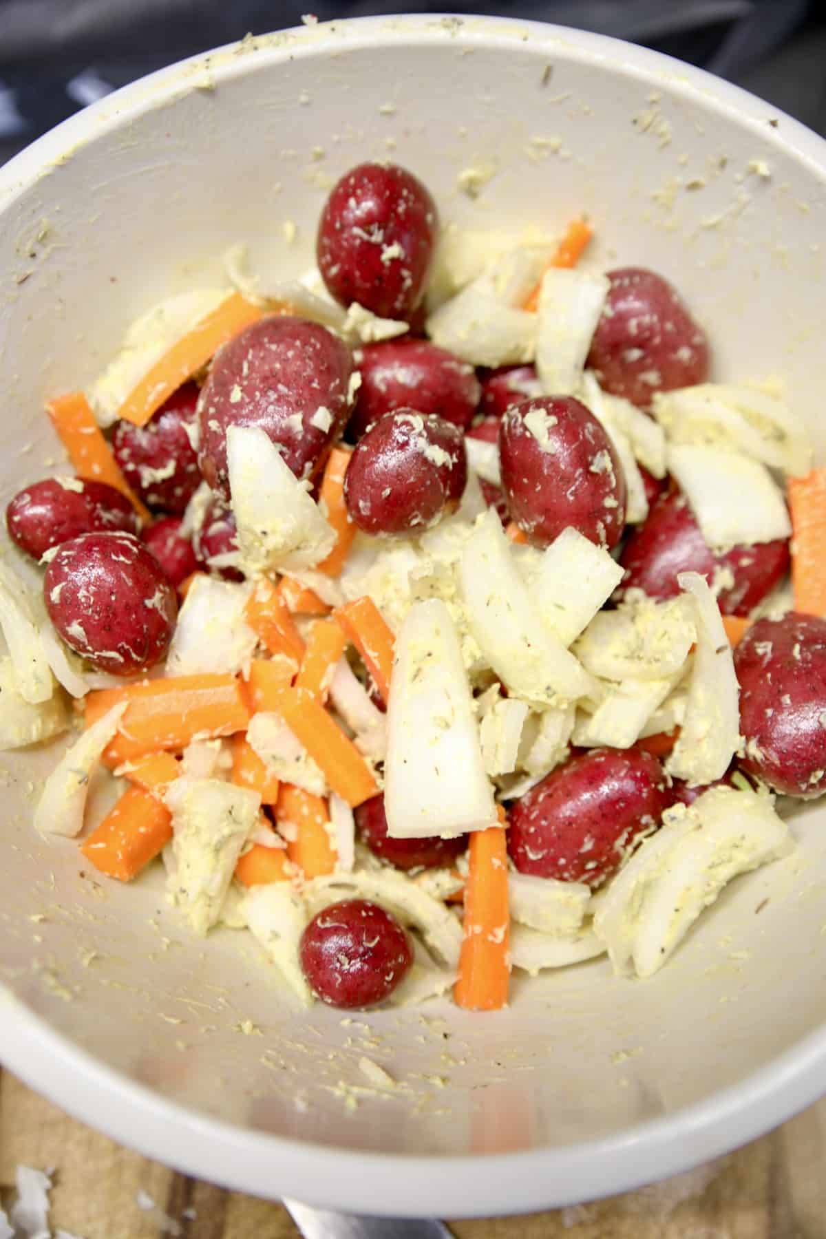 Bowl of potatoes, onions, carrots with butter and seasonings.