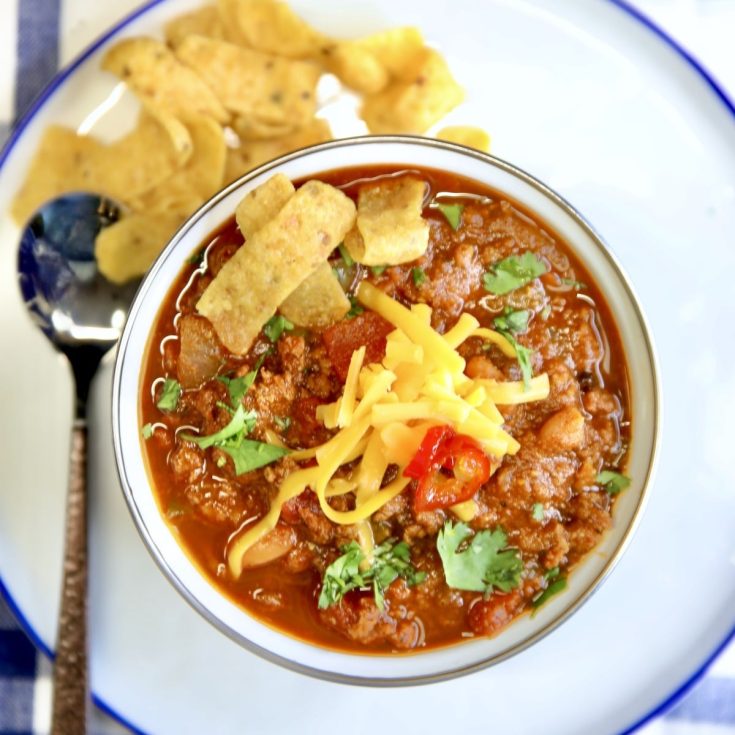 Bowl of chili with shredded cheese, fritos and jalapenos.