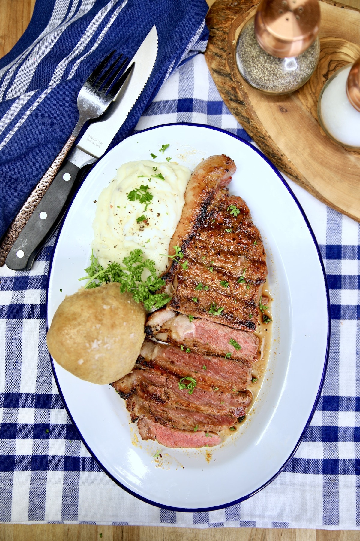 Strip Steak with roll and mashed potatoes on a platter.
