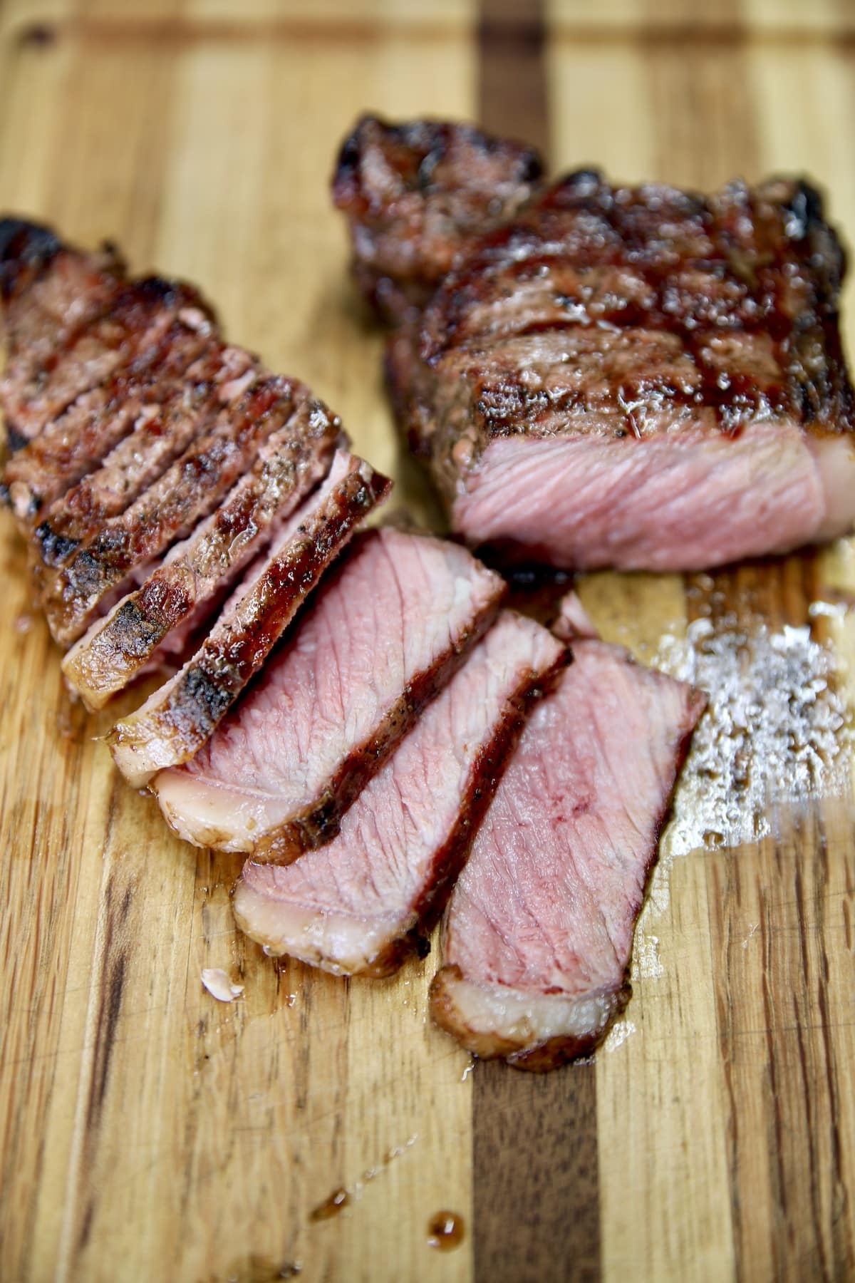Cutting board with grilled NY Strip Steak, partially sliced.