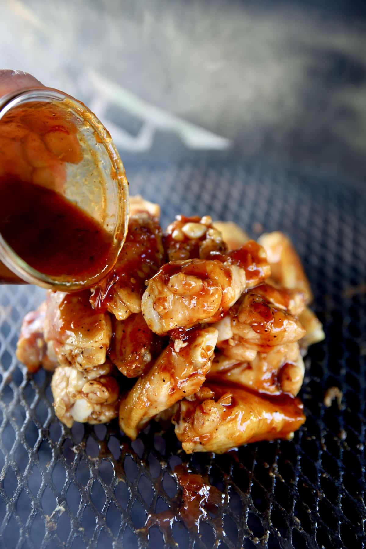 Pouring bbq sauce over wings on the grill.