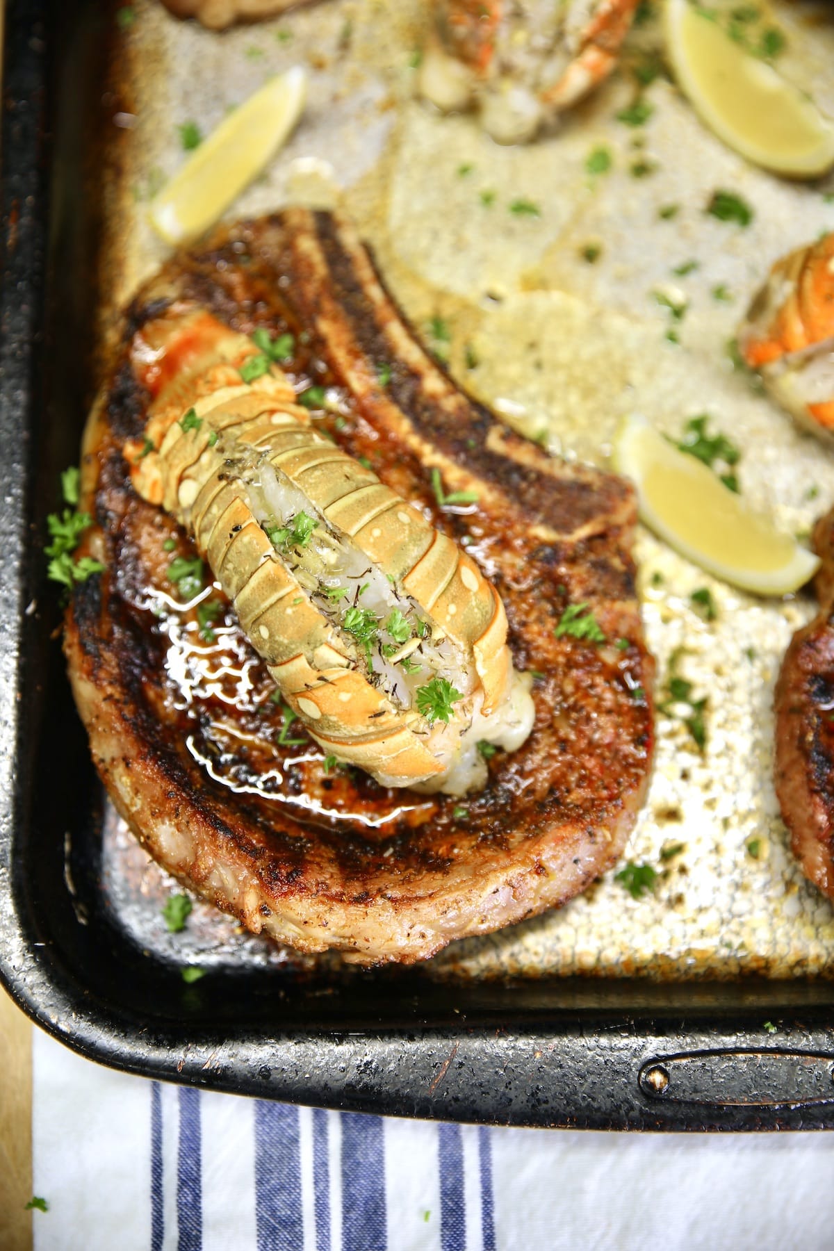 Closeup of grilled ribeye topped with lobster tail. Lemon slices.
