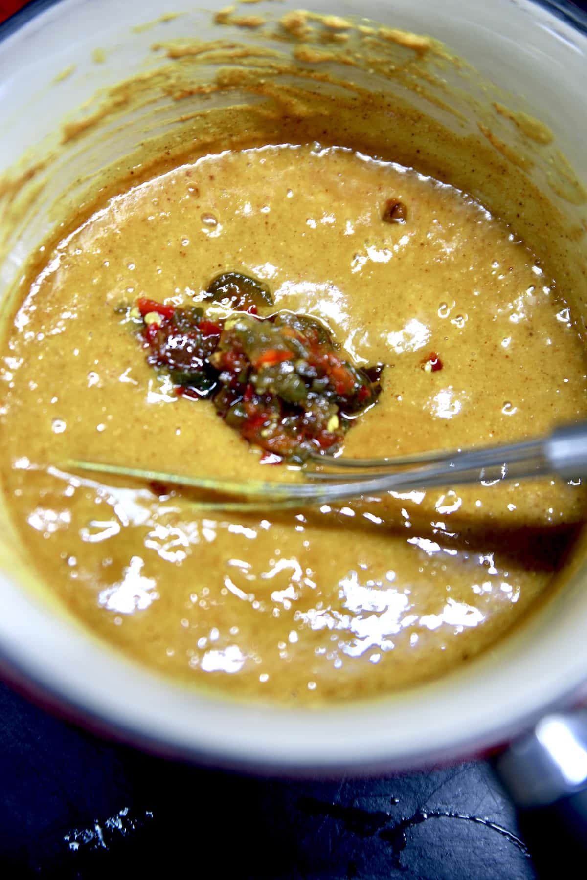 Mustard sauce in a pan with diced jalapenos.
