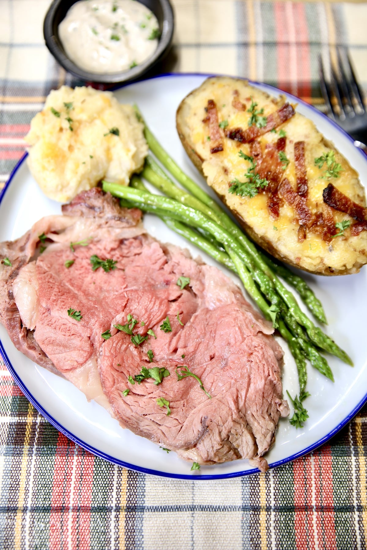 Plate of prime rib, twice baked potato, asparagus, biscuit.