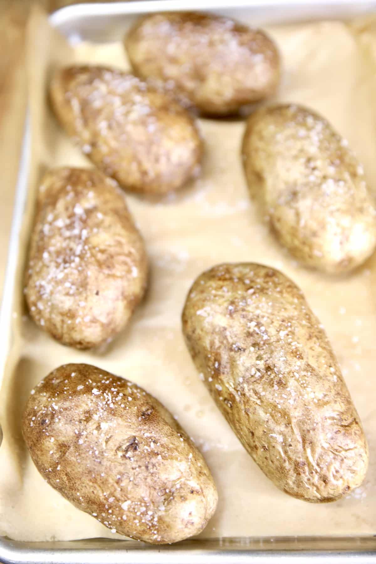 6 baked potatoes on a baking sheet.