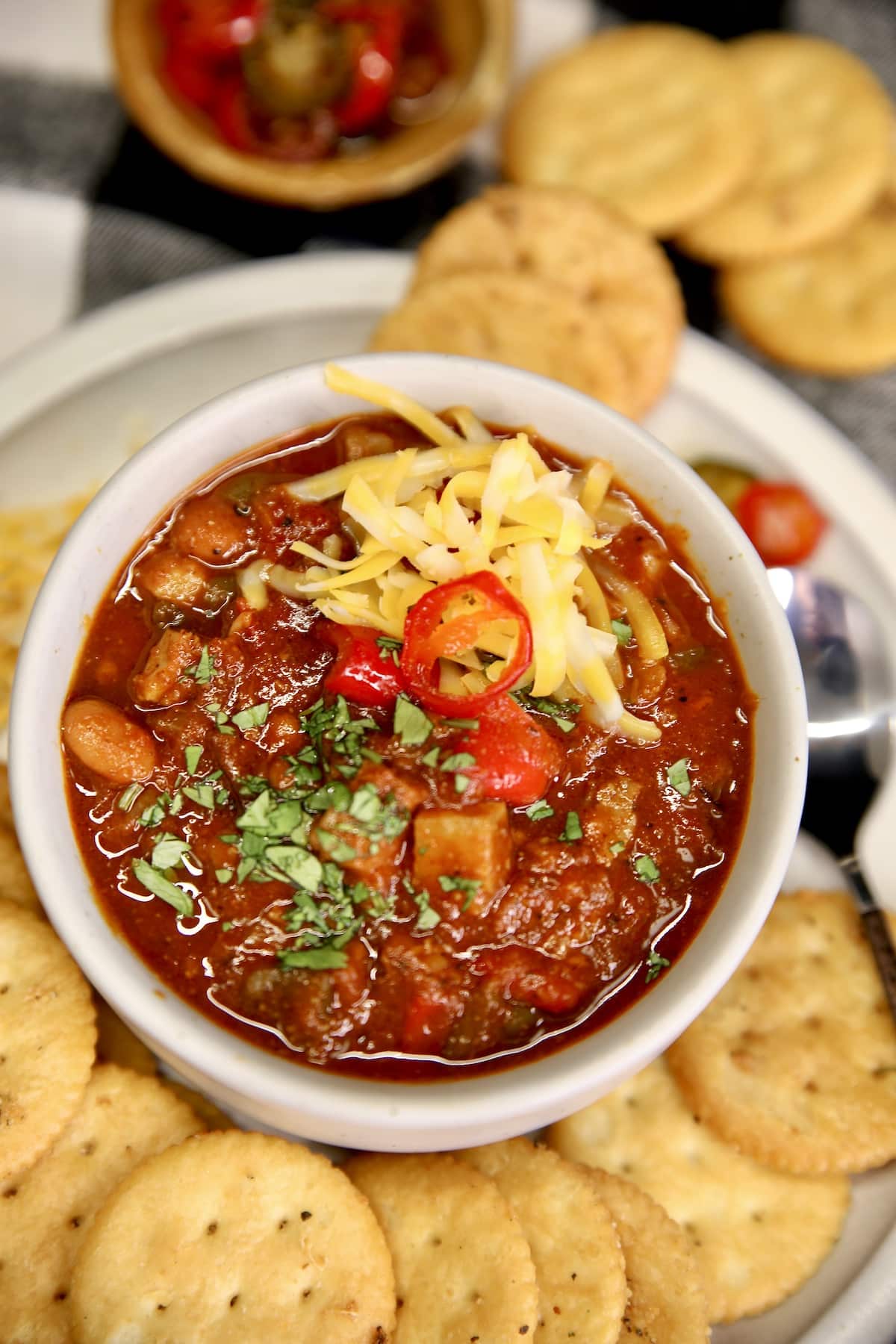Brisket Chili in a bowl with shredded cheese, on a plate with crackers.