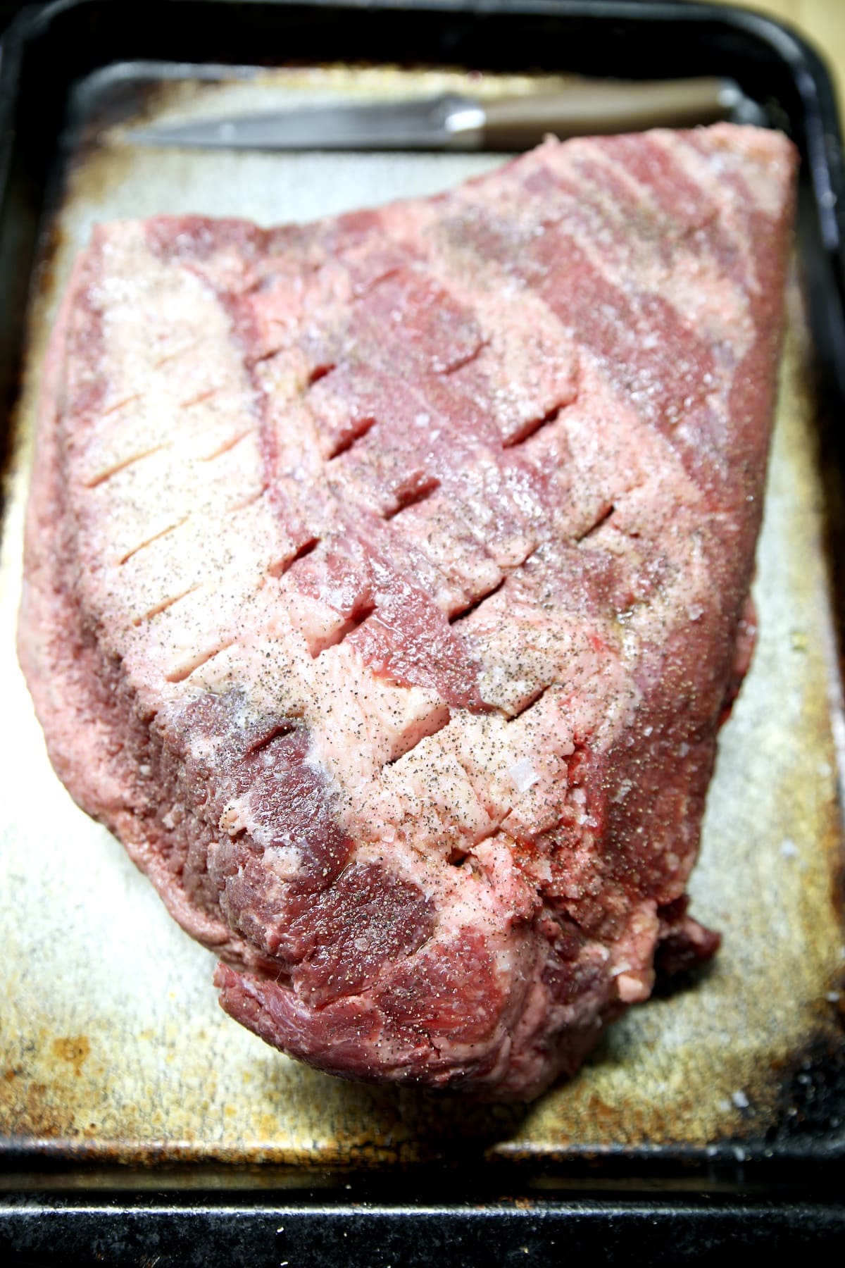 Raw brisket point on a sheet pan, pierced with knife.