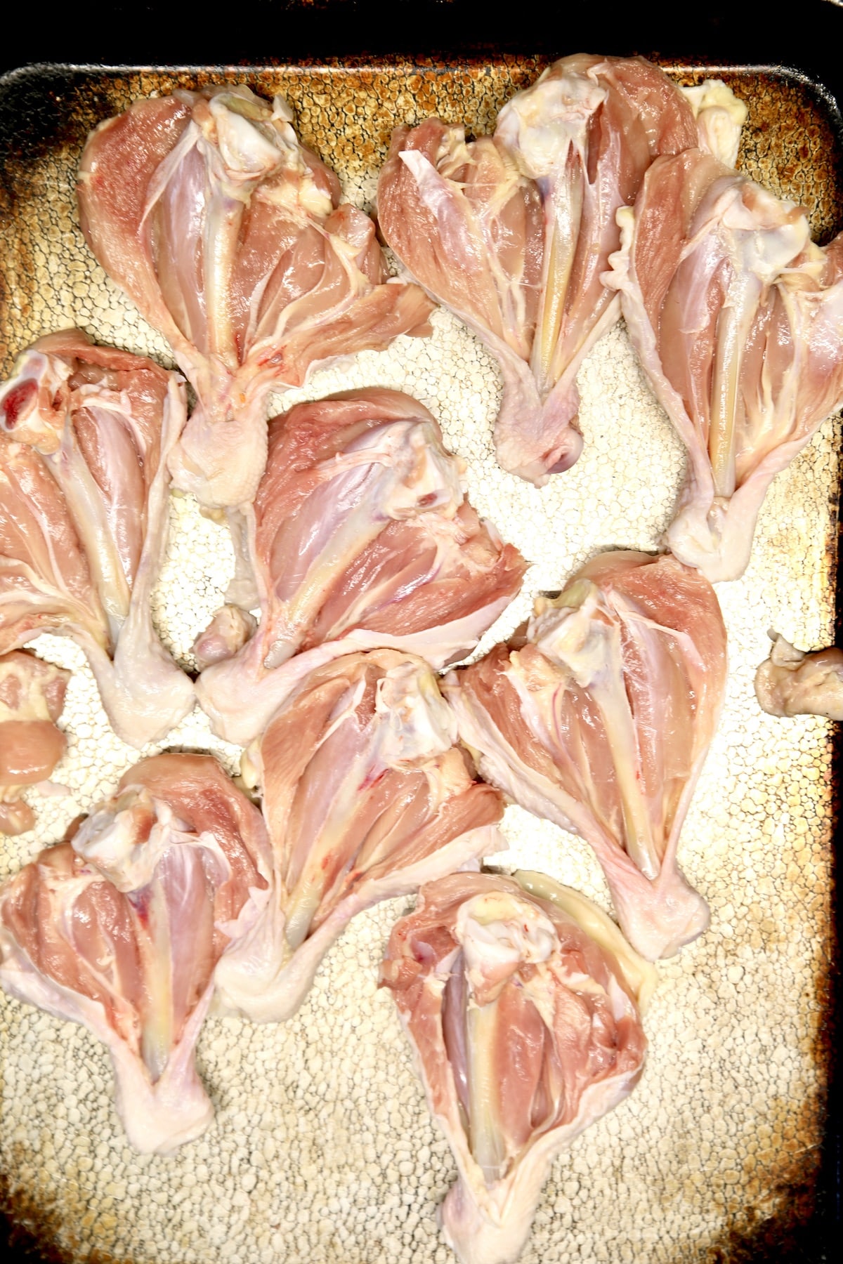Raw butterflied chicken legs on a sheet pan.