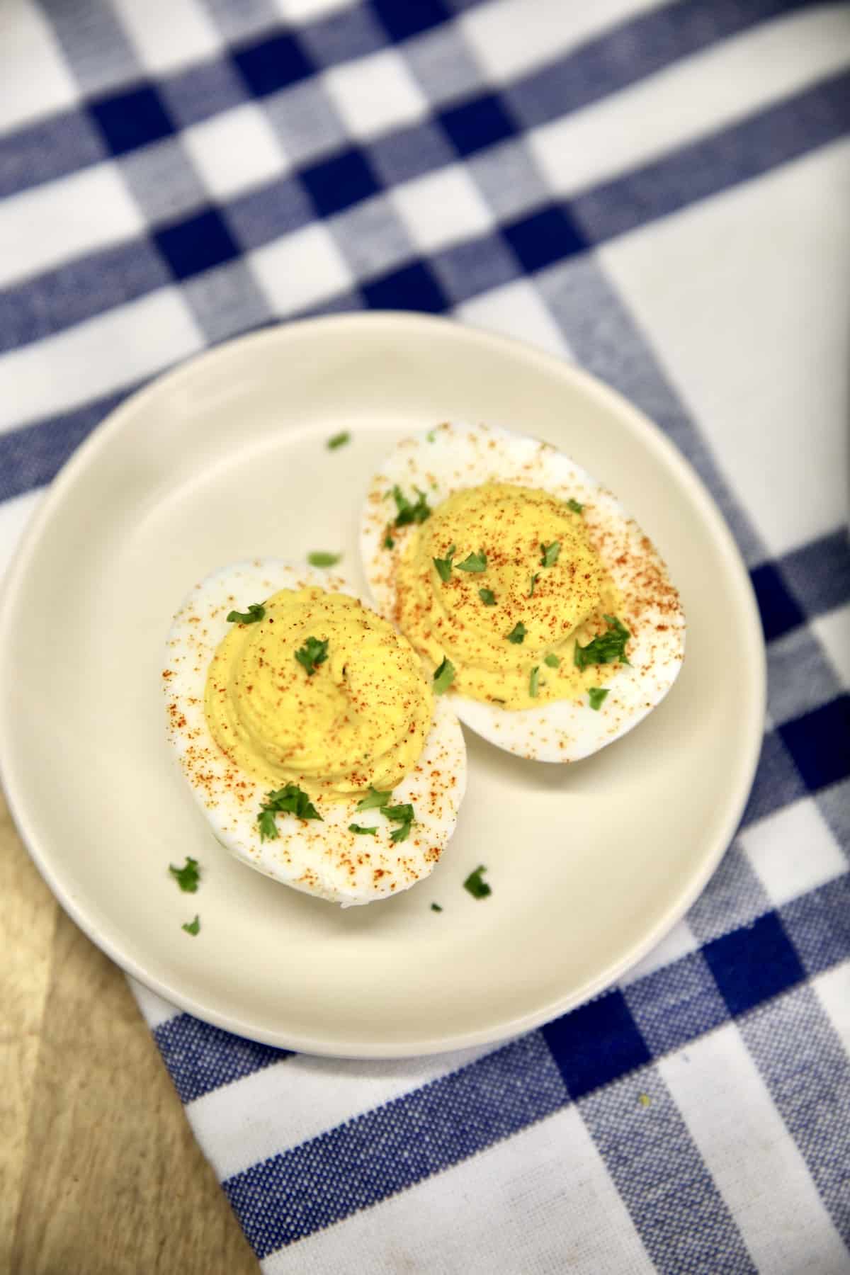 Small appetizer plate with 2 deviled eggs on a blue and white napkin.
