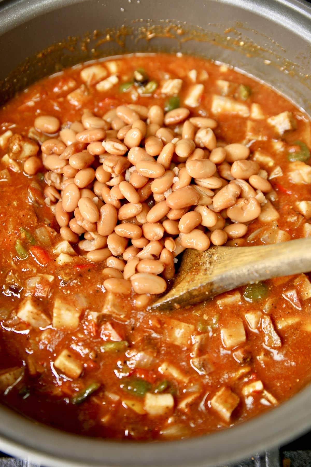 Adding pinto beans to pan of chili, wooden spoon.