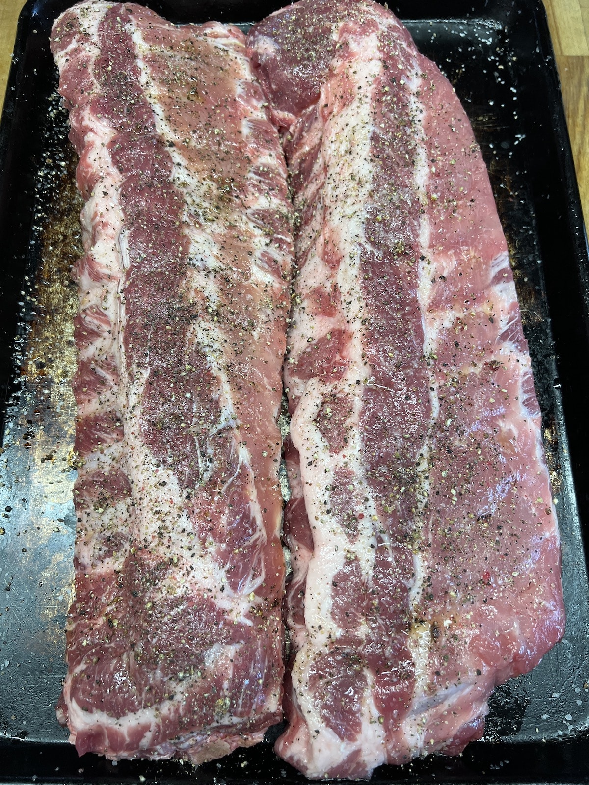 2 racks ribs on a sheet pan with salt & pepper.