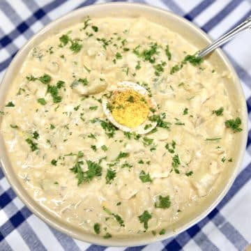 Bowl of potato salad with parsley garnish, egg in center.