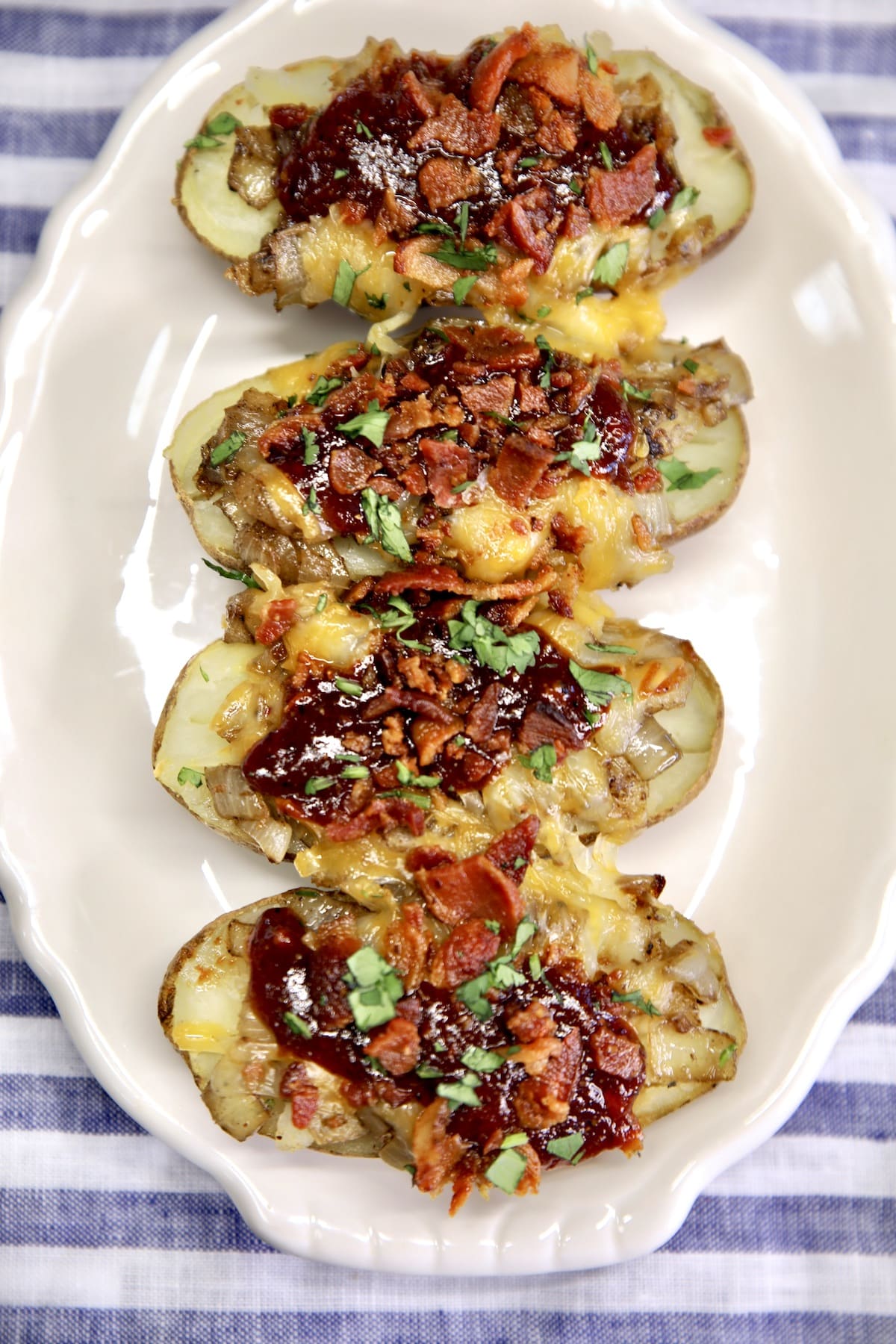 Platter of 4 baked potato halves topped with cheese, bbq sauce and bacon.