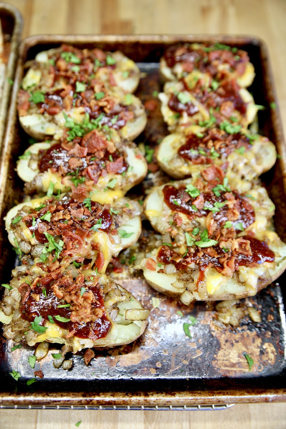 Sheet pan of baked potatoes topped with bacon, cheese, bbq sauce.