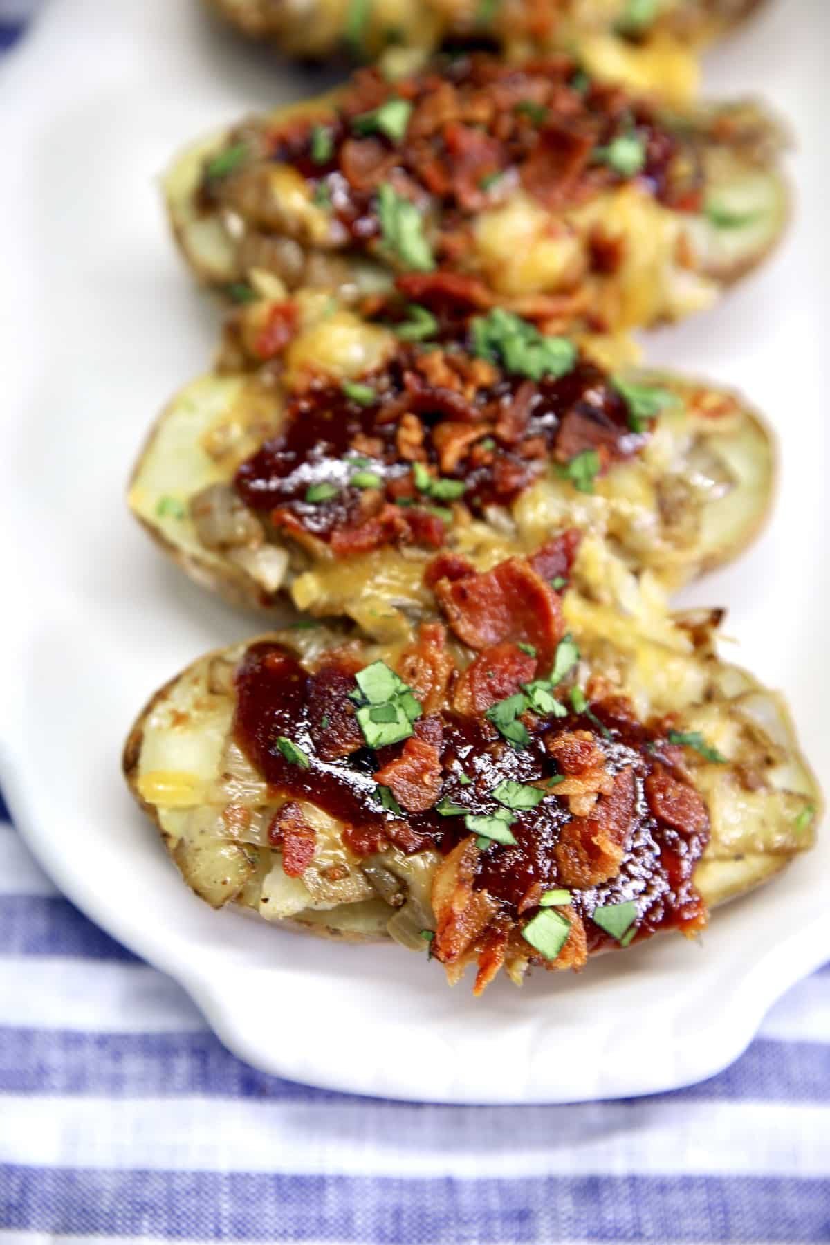 Platter of baked potatoes with bacon, bbq sauce, cheese.