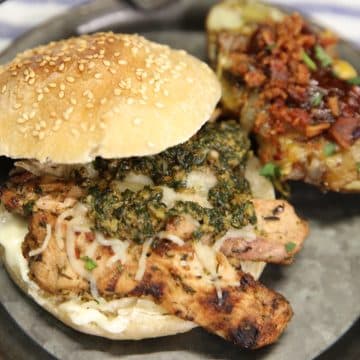 Grilled chicken sandwich on a plate with pesto and melted cheese.