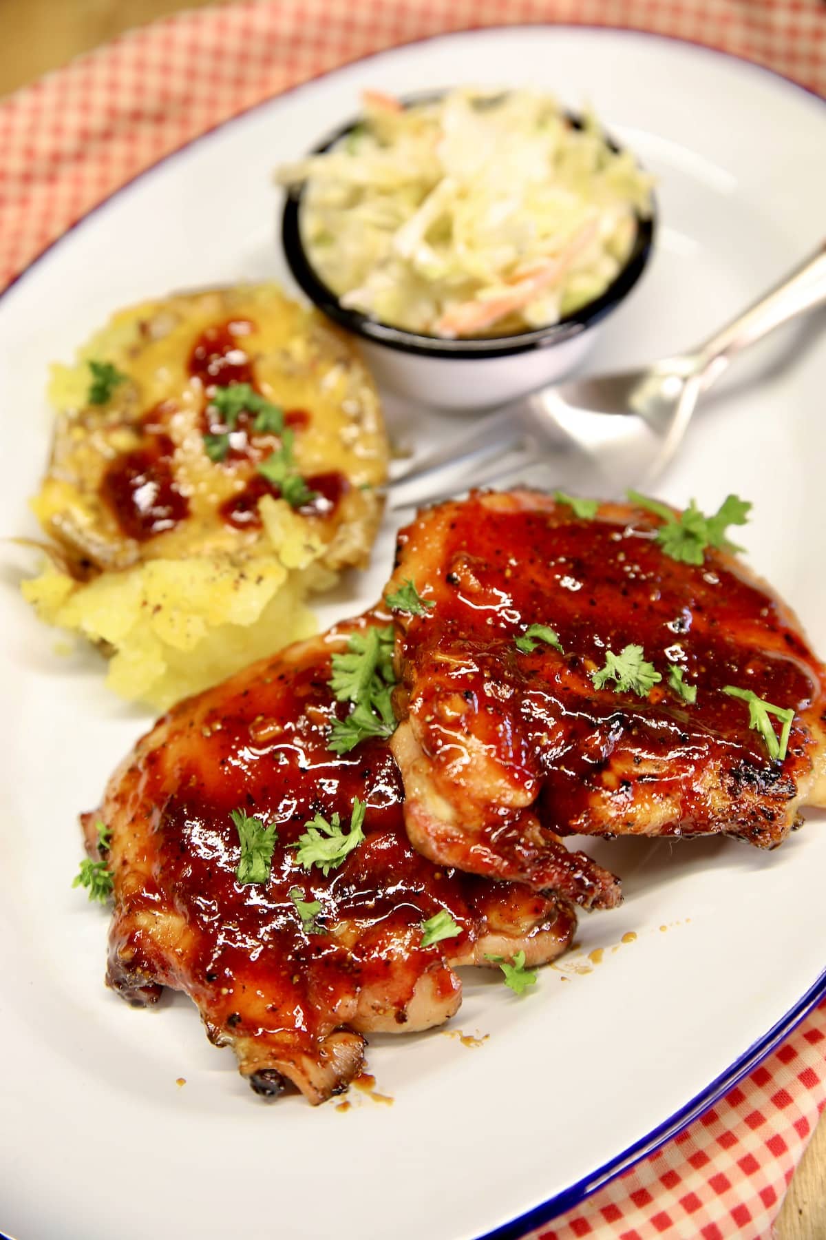 2 bbq chicken thighs on a plate with potato and slaw.