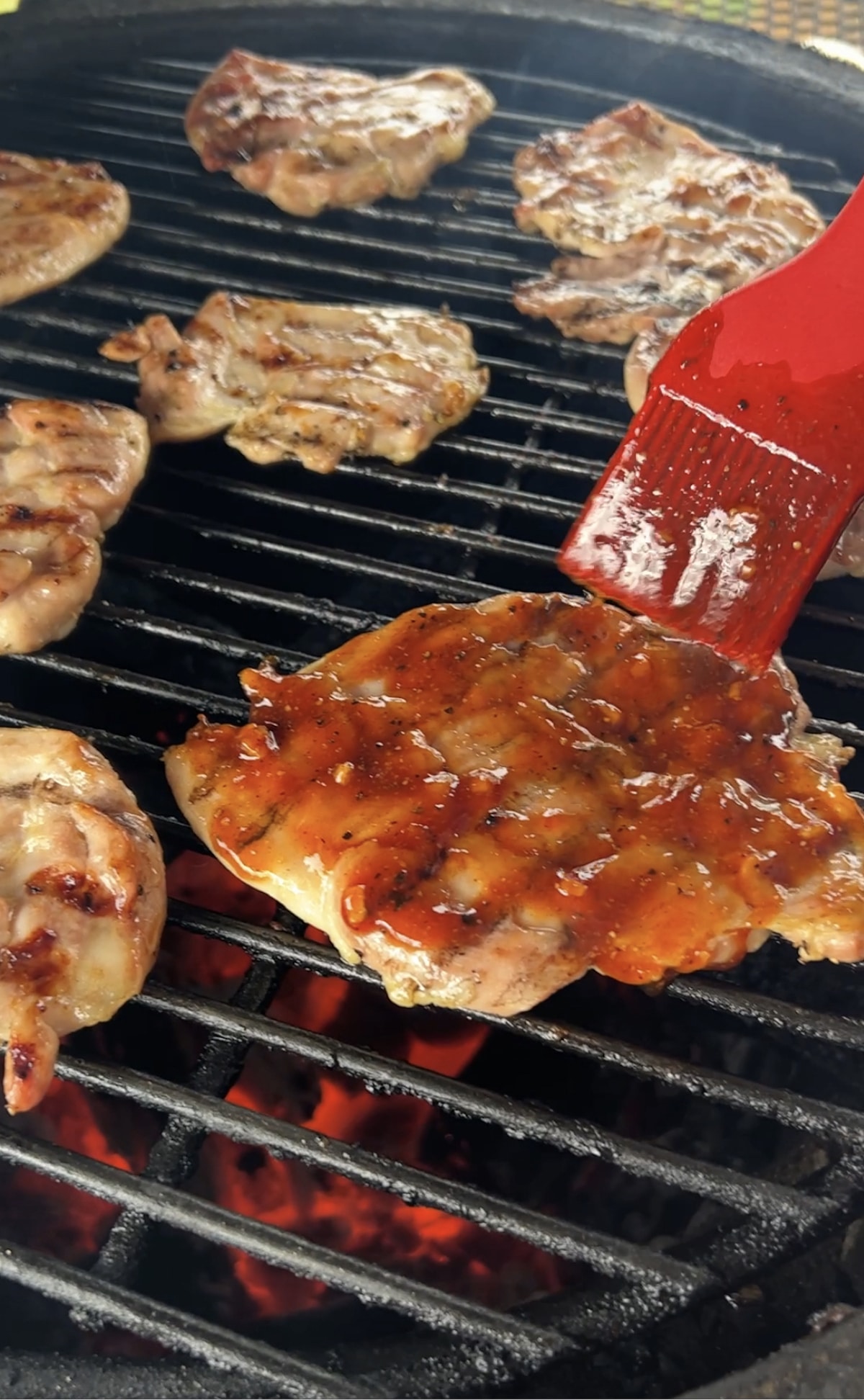 Brushing BBQ sauce onto chicken thighs on grill.