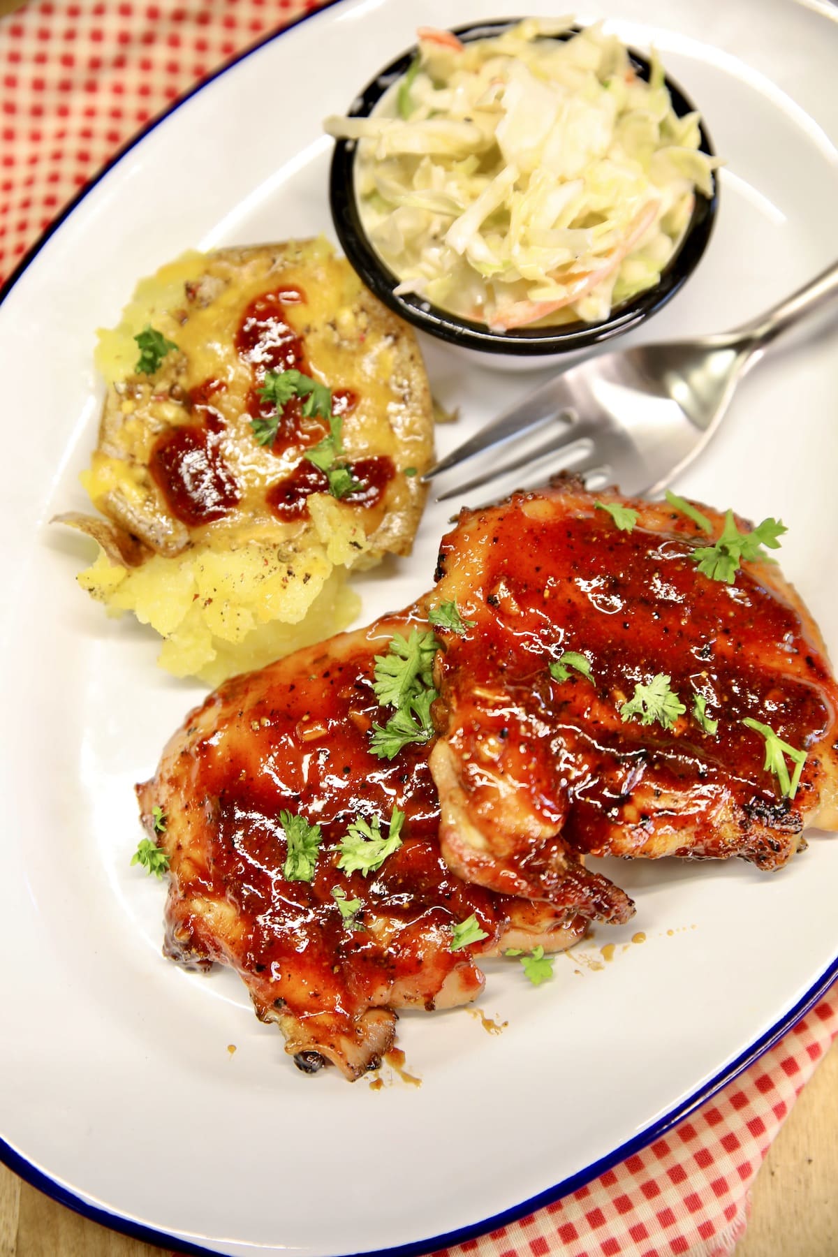 BBQ Chicken thighs on a plate with slaw and potato.