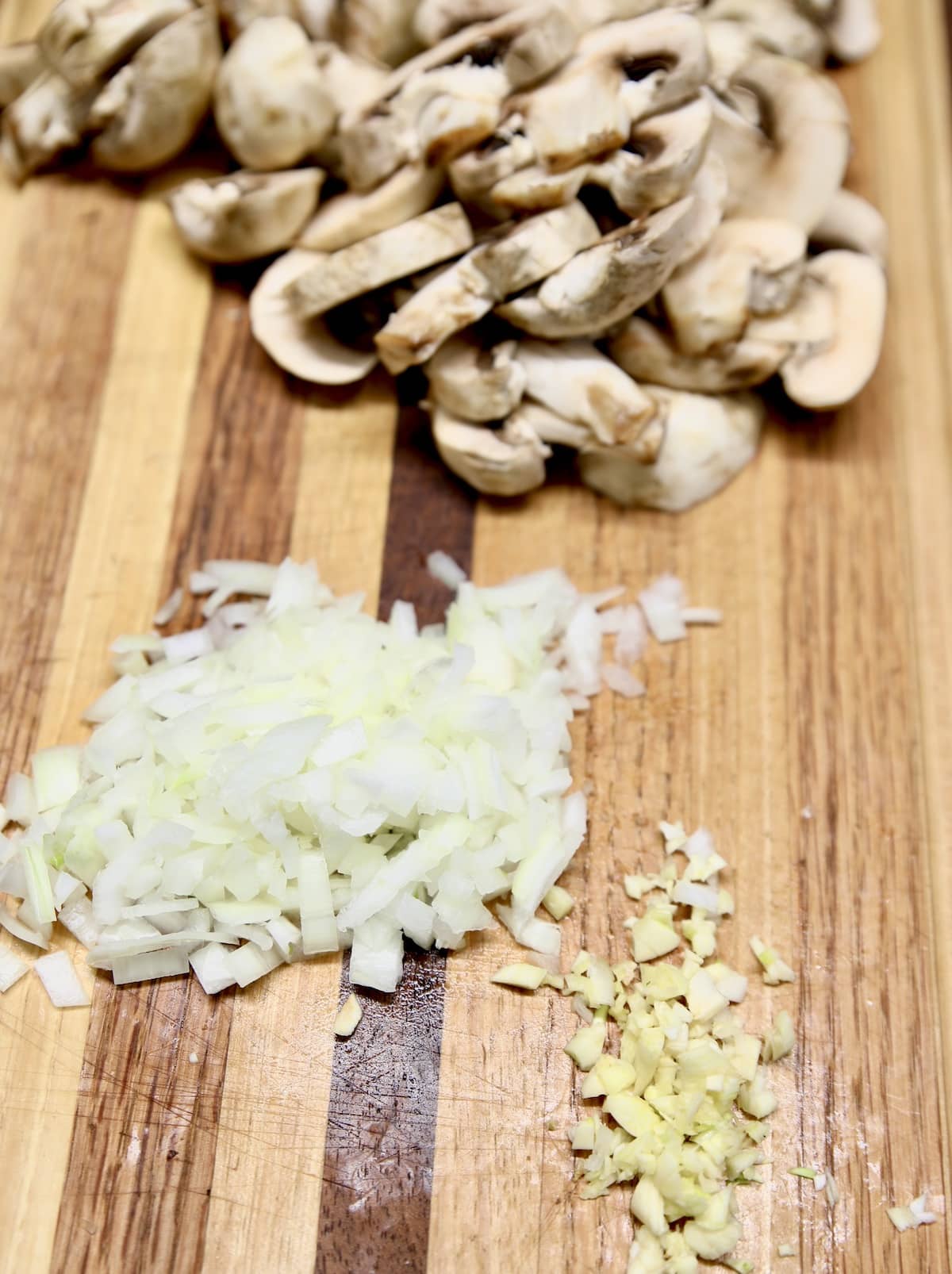 Diced onions and minced garlic on a cutting board with sliced mushrooms.