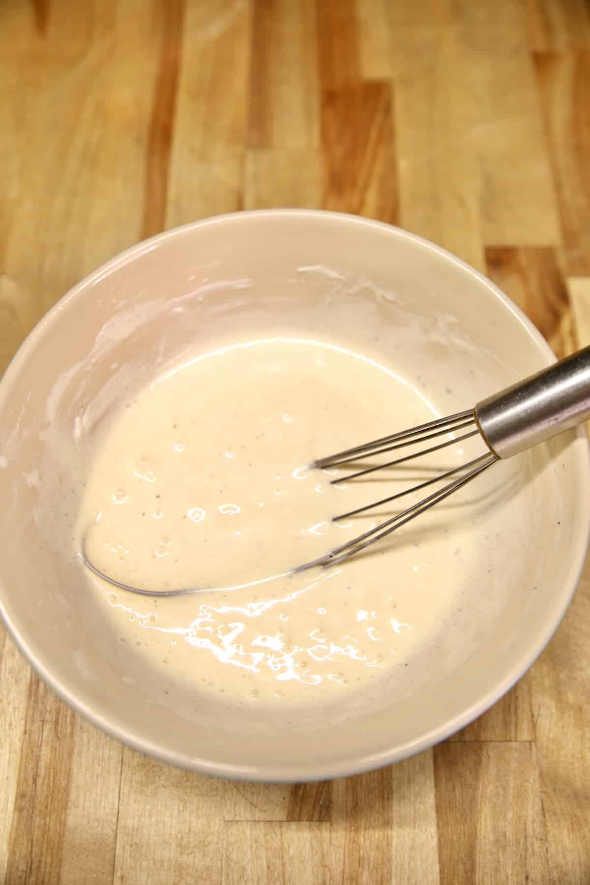 Coleslaw dressing in a bowl with a whisk.