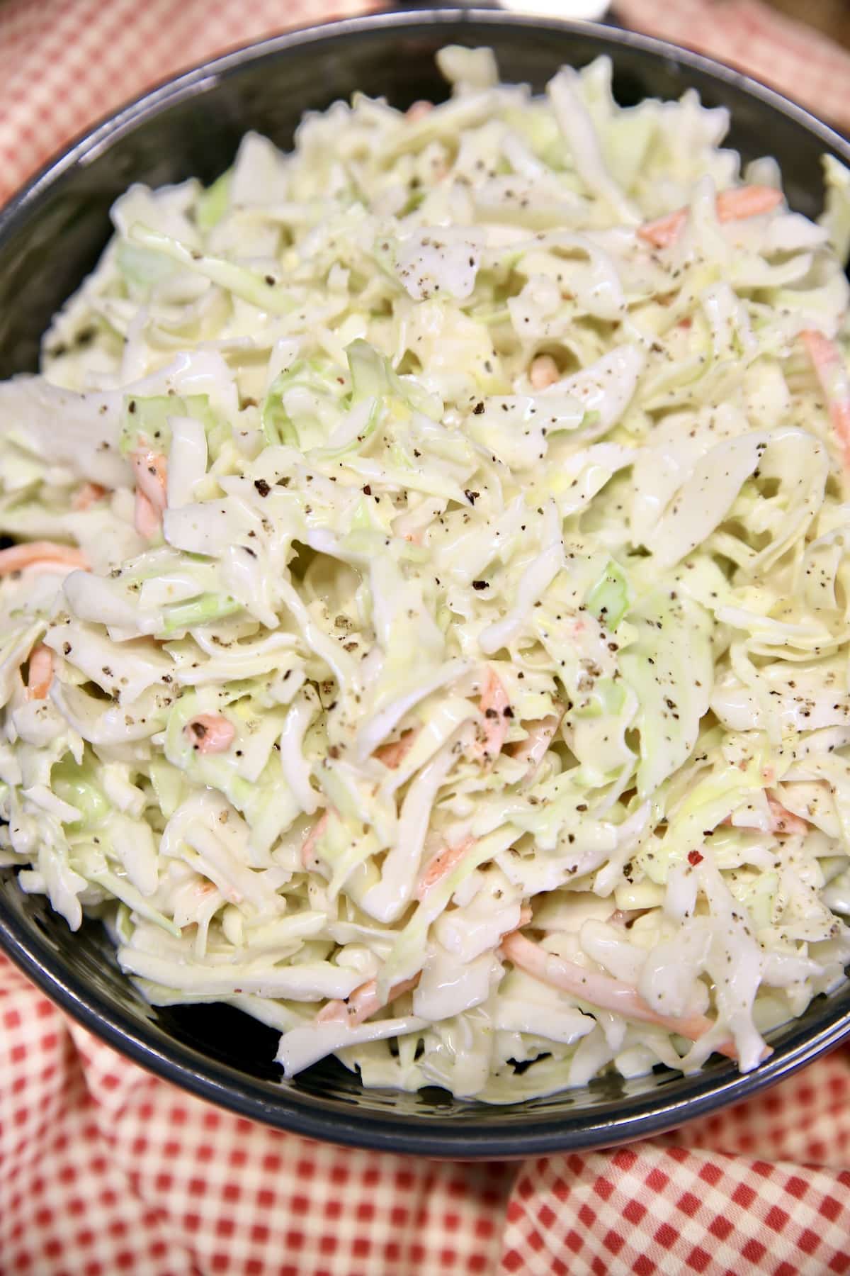 Coleslaw in a black bowl on red check napkin.